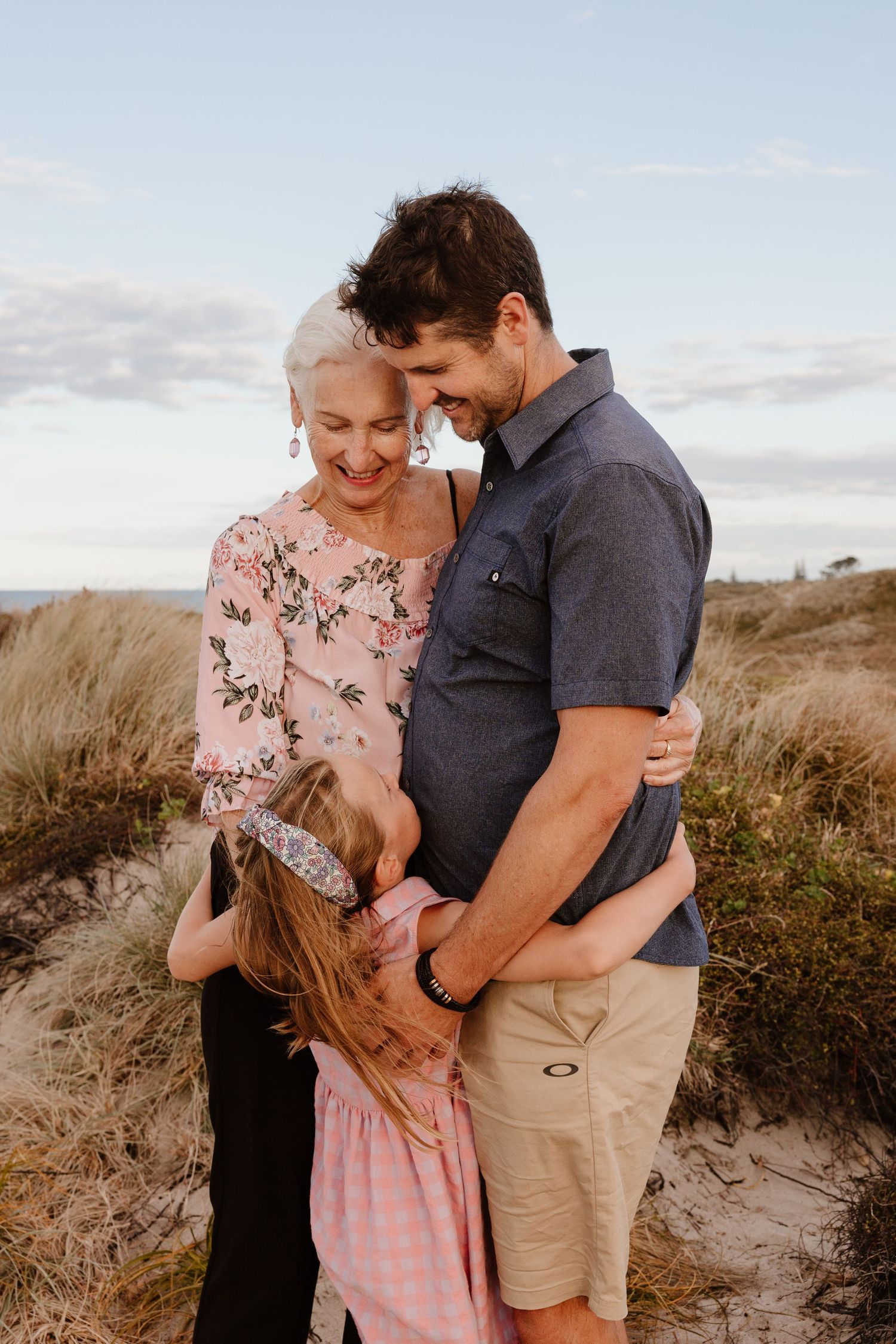 Three generations share an intimate moment on coastal hilltop during golden hour.