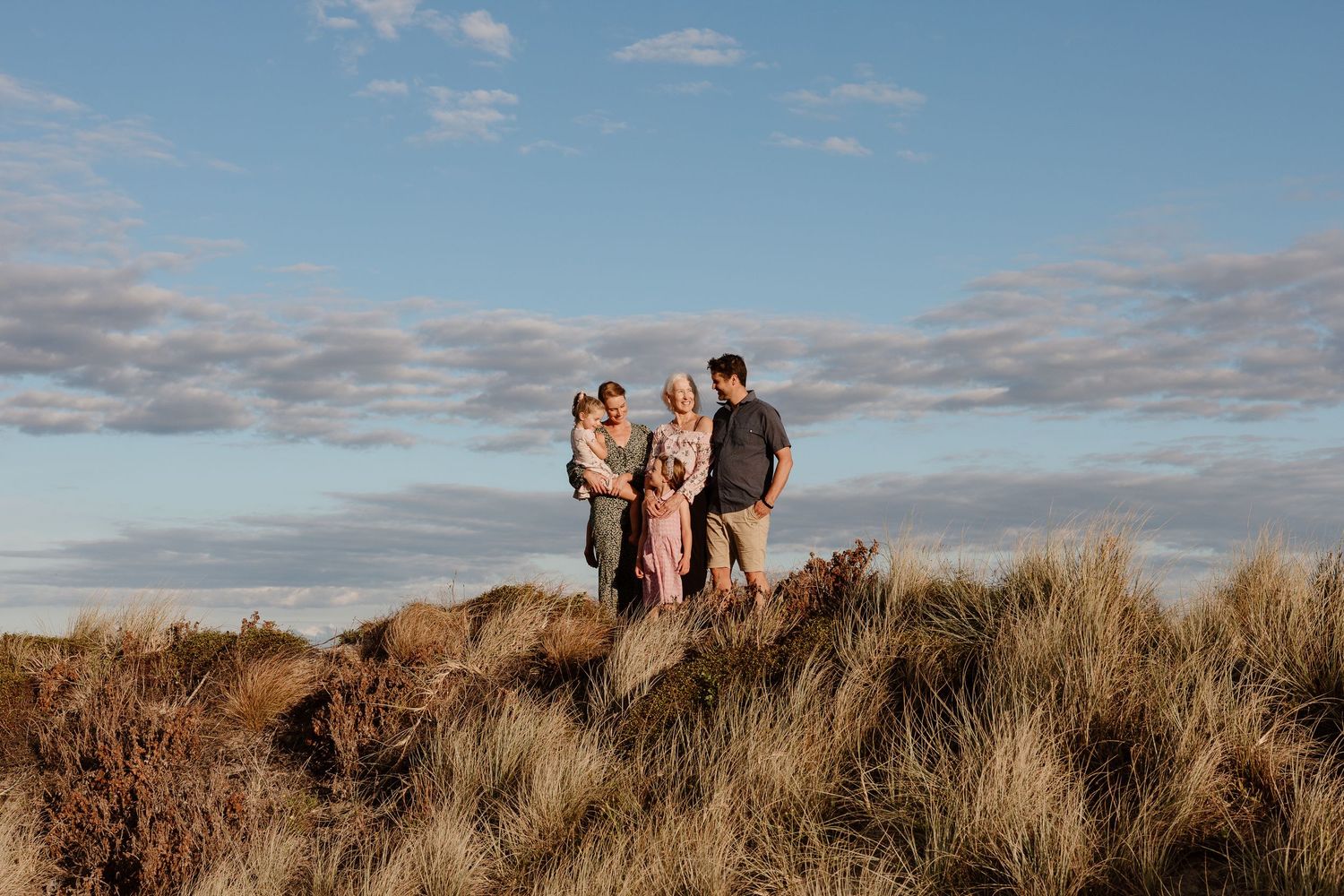 Family standing together on grassy coastal dunes at sunset.