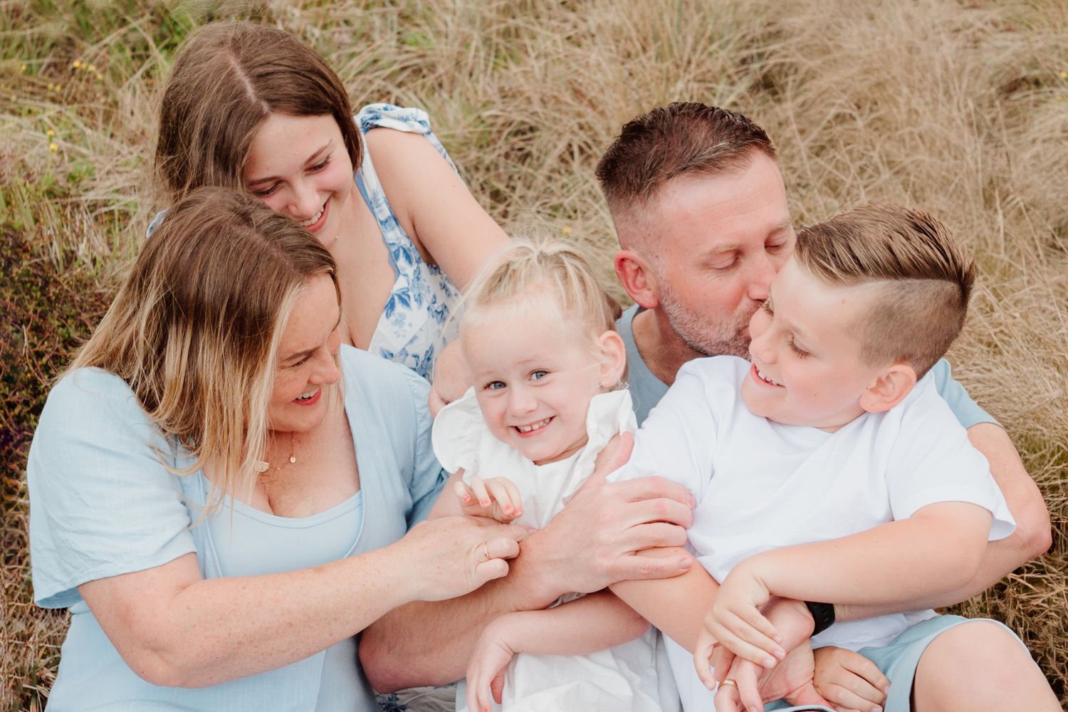 A candid family moment captured in golden sunlight amidst wild coastal grasses.