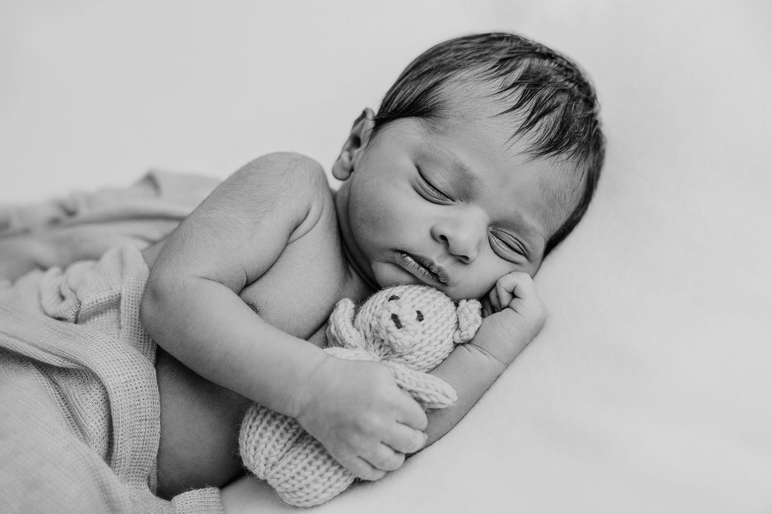 Sleeping newborn baby photographed in artistic monochrome style.