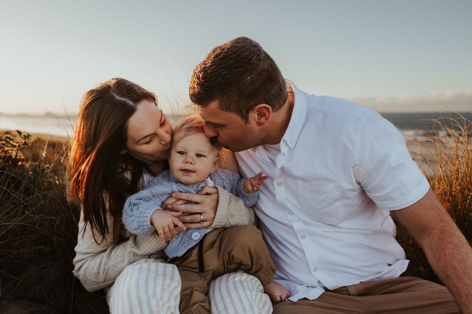 Family cuddles together on beach during golden hour sunset.