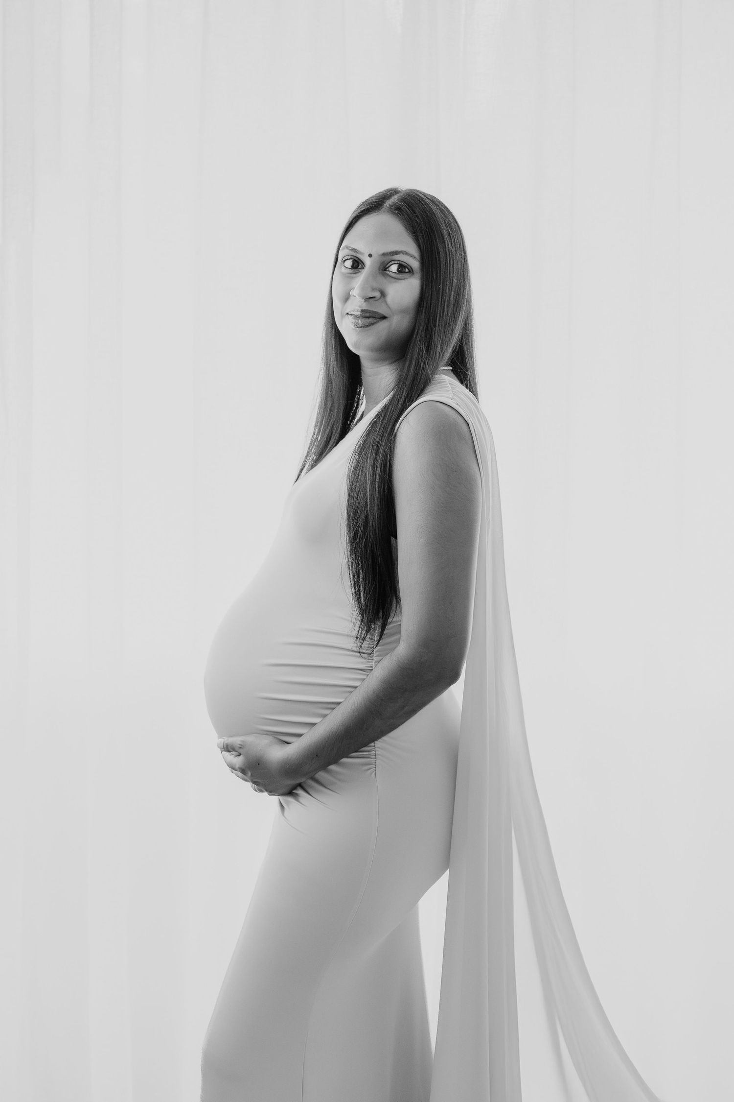 Minimalist studio maternity portrait in black and white against plain backdrop.