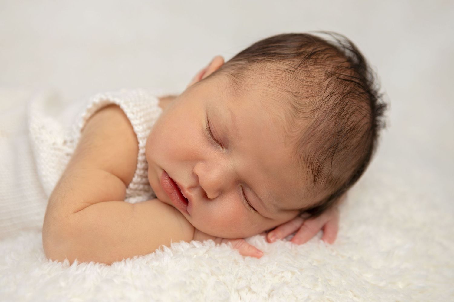 Peaceful newborn sleeping on white textured blanket in studio setting.