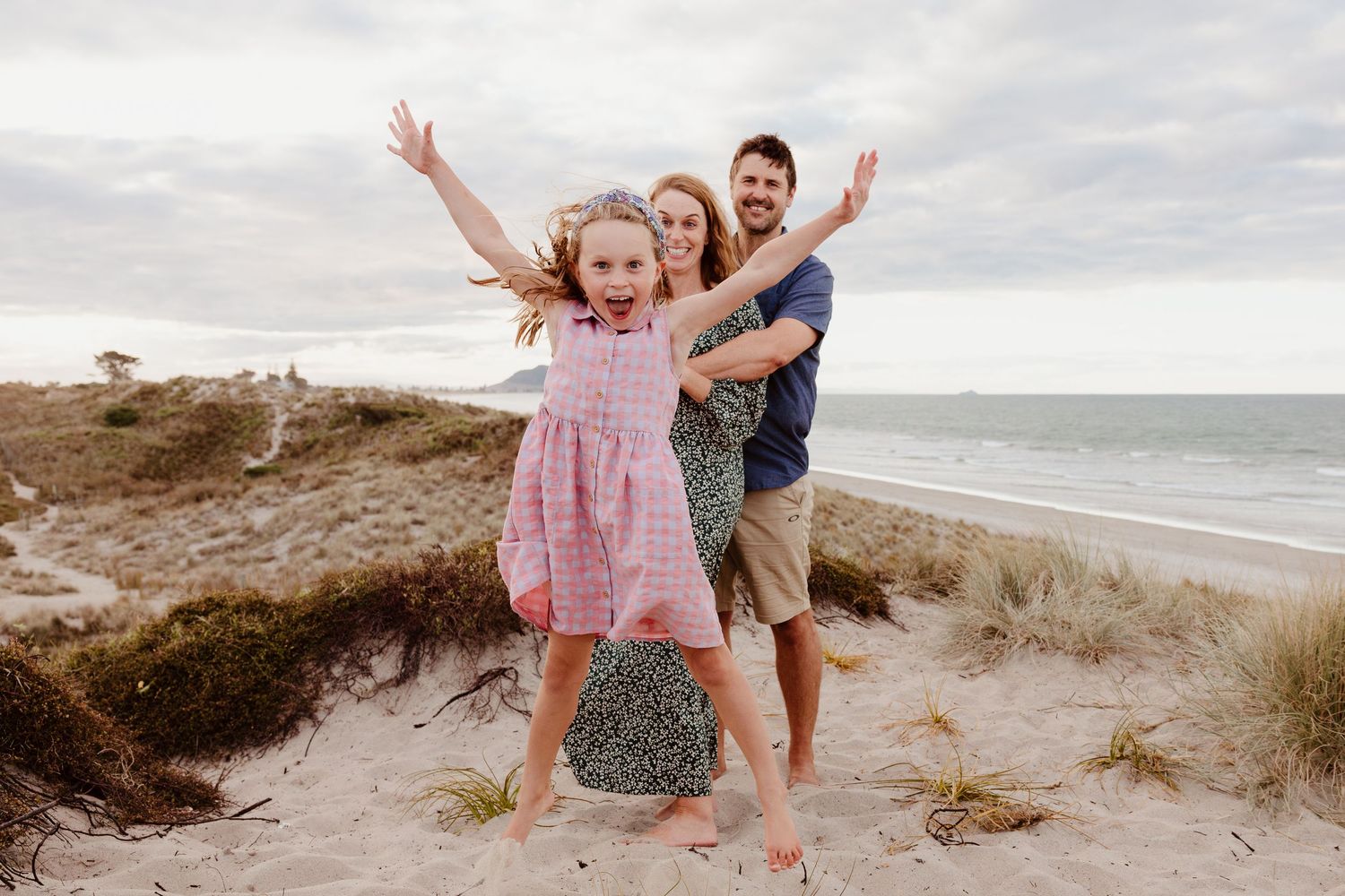 Joyful family playing and jumping on sandy beach dunes.