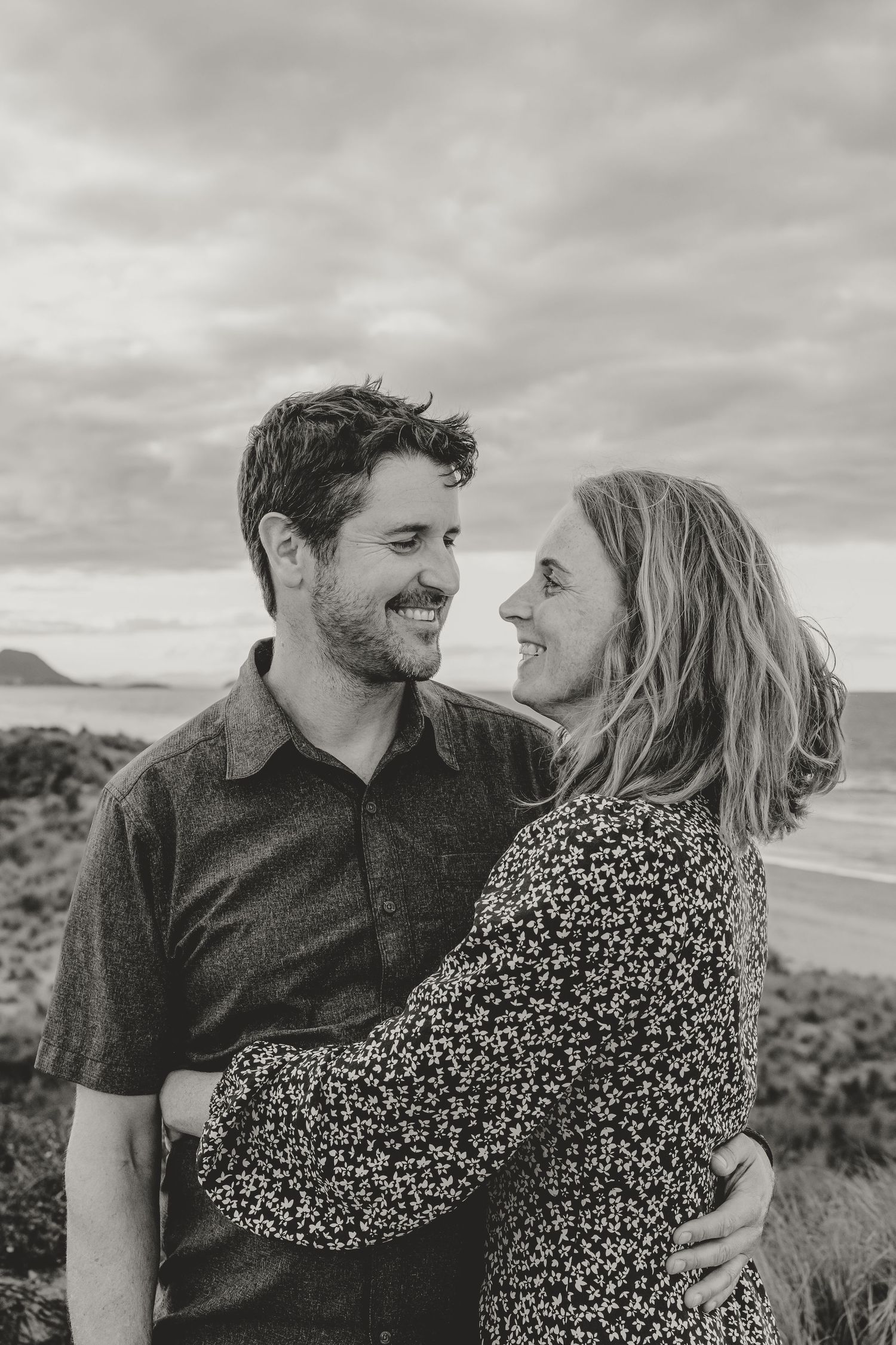 Couple sharing intimate moment on coastal cliff with ocean view in black and white.