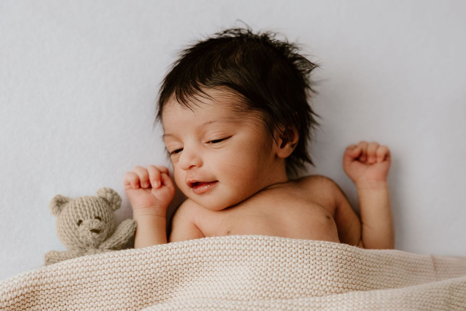 Newborn baby in white blanket sleeping peacefully with a soft teddy bear companion.