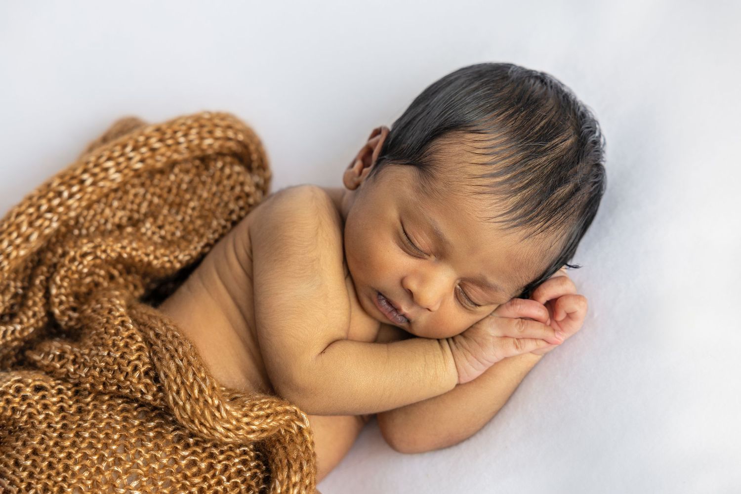 Sleeping newborn wrapped in brown knit blanket during professional photo shoot.