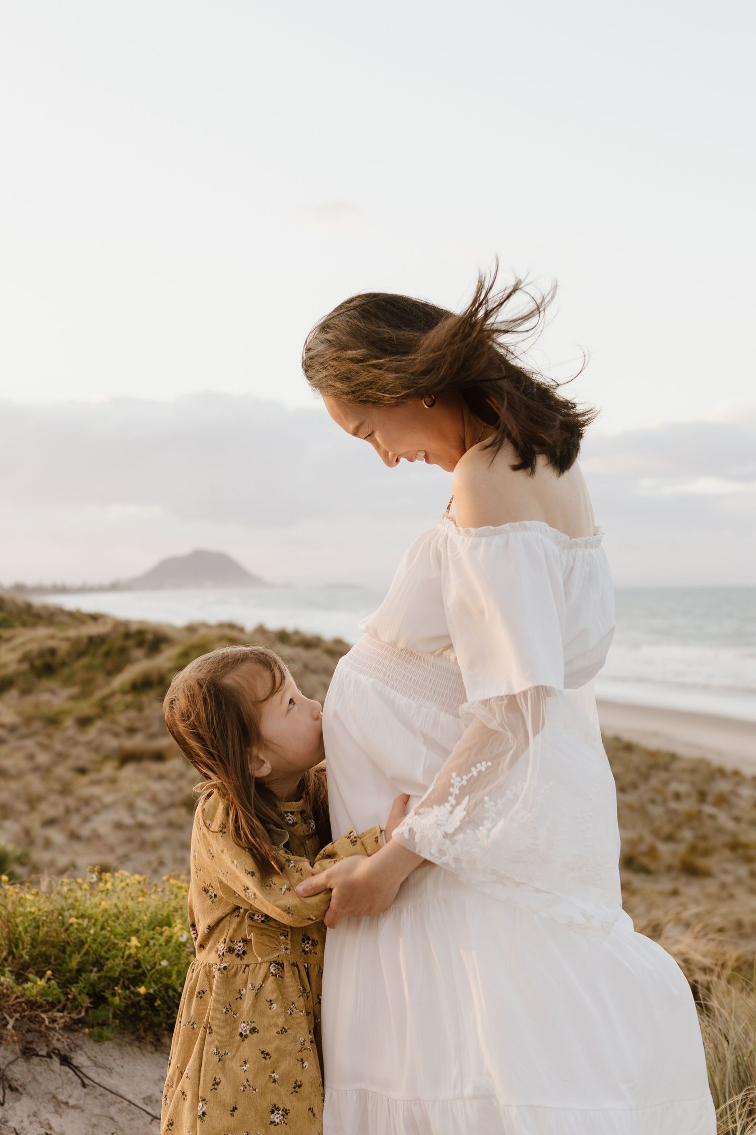 Tender beach maternity photos with child touching baby bump.