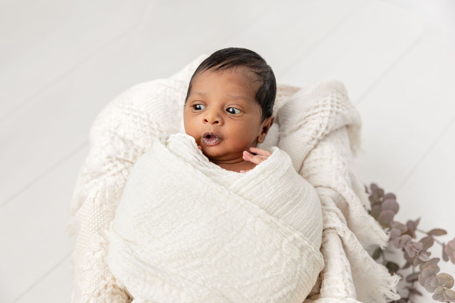 Newborn baby wrapped in white blanket lying on side with peaceful expression.