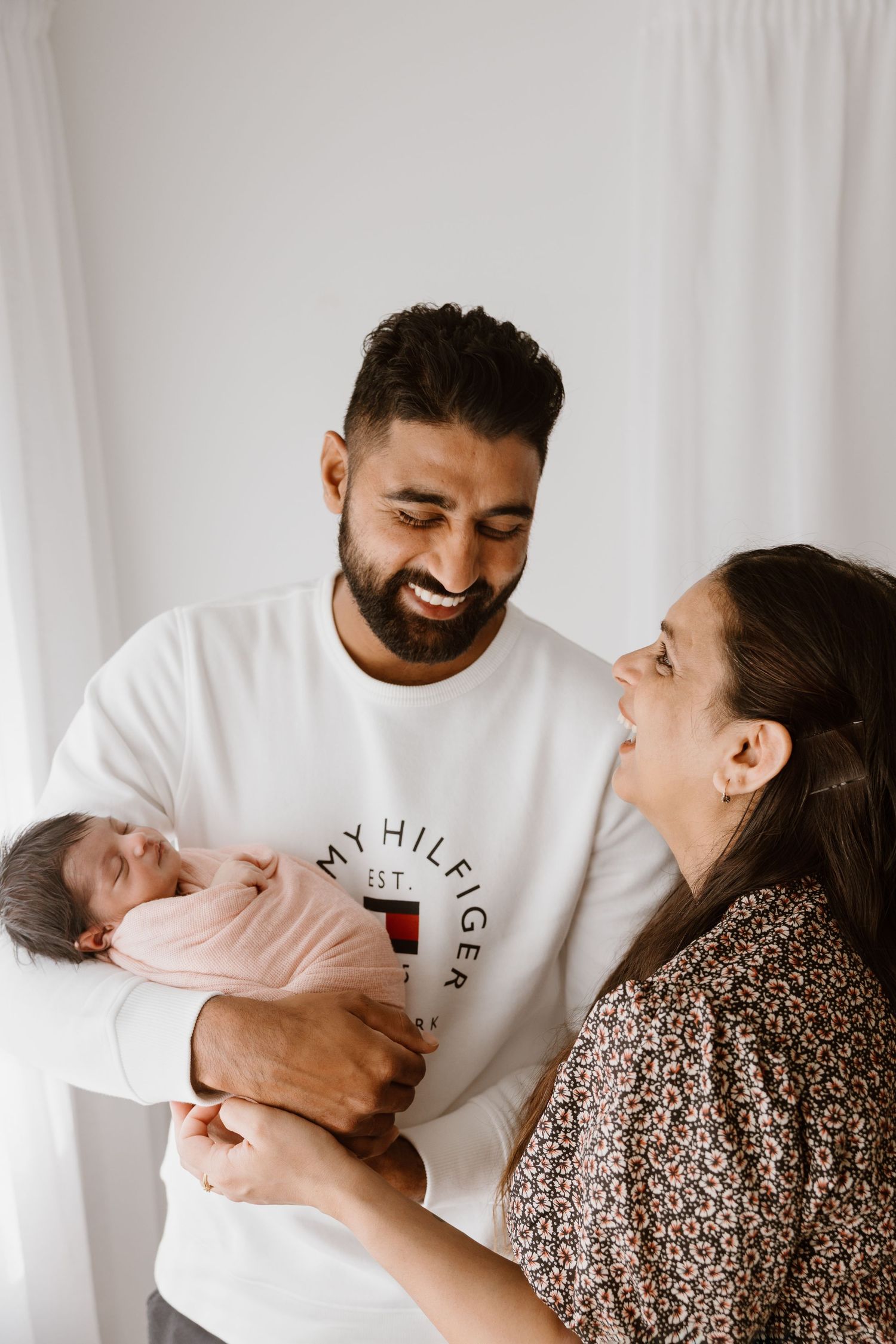A joyful family moment with their newborn baby against a white backdrop.