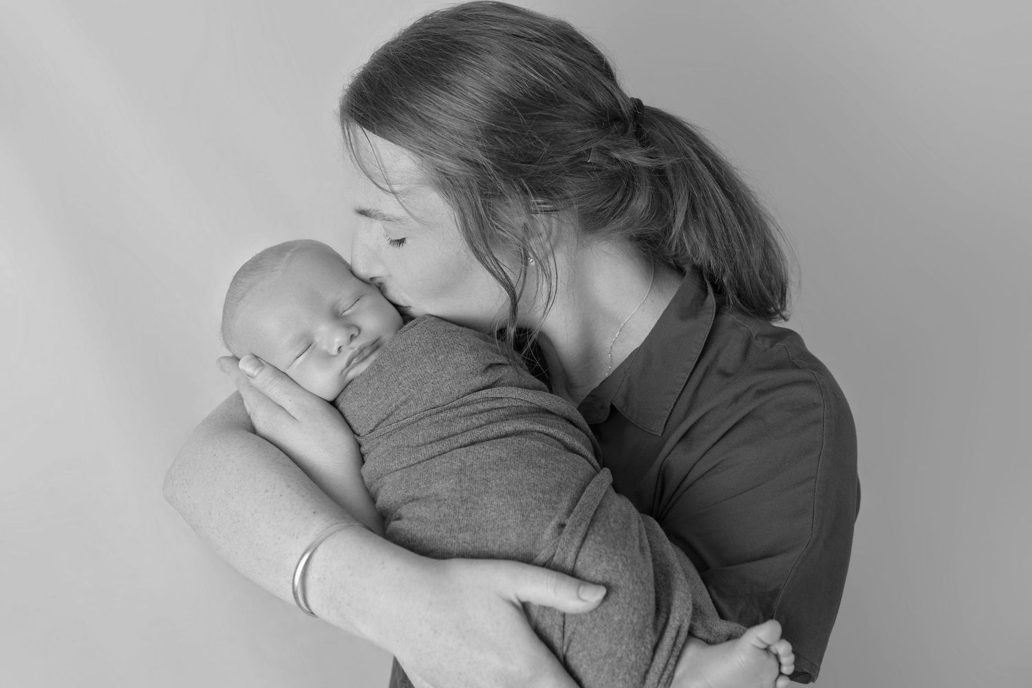 An intimate black and white portrait of parent kissing their swaddled baby.