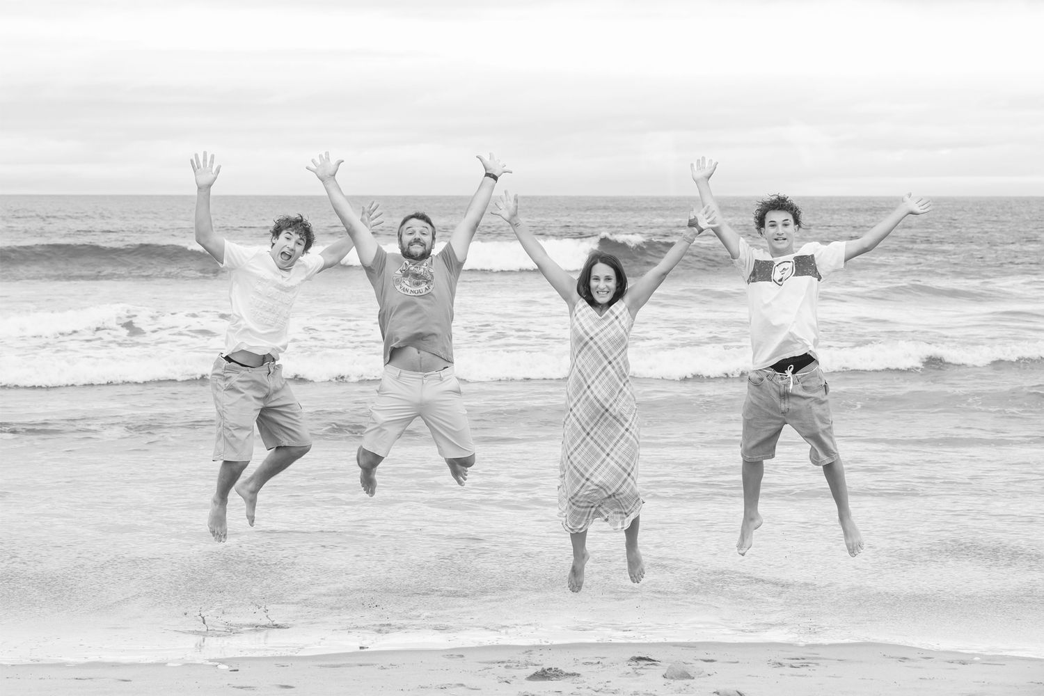 Group jumping joyfully together on beach in black and white photo.