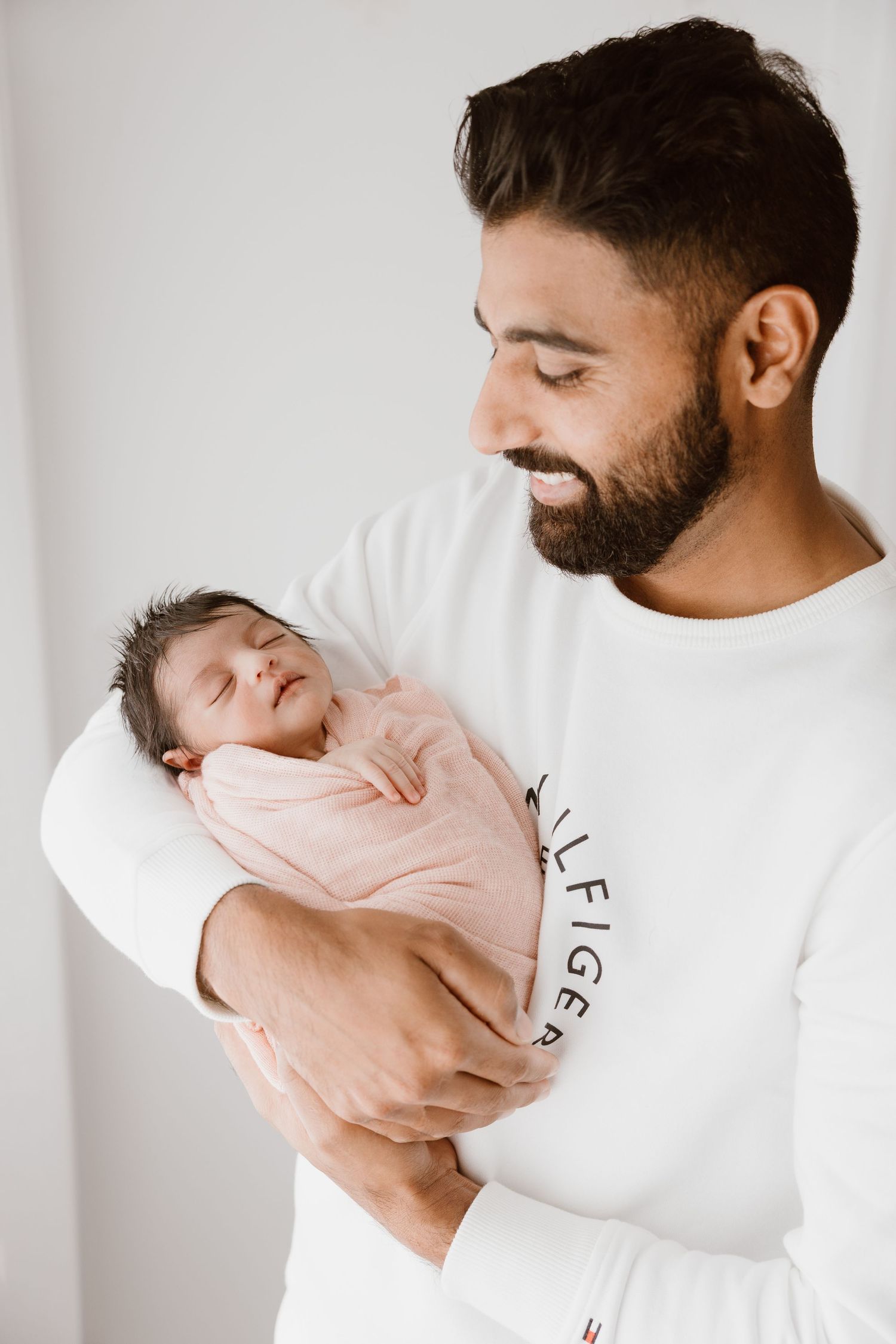 A tender moment between parent and sleeping newborn baby in a pink swaddle.