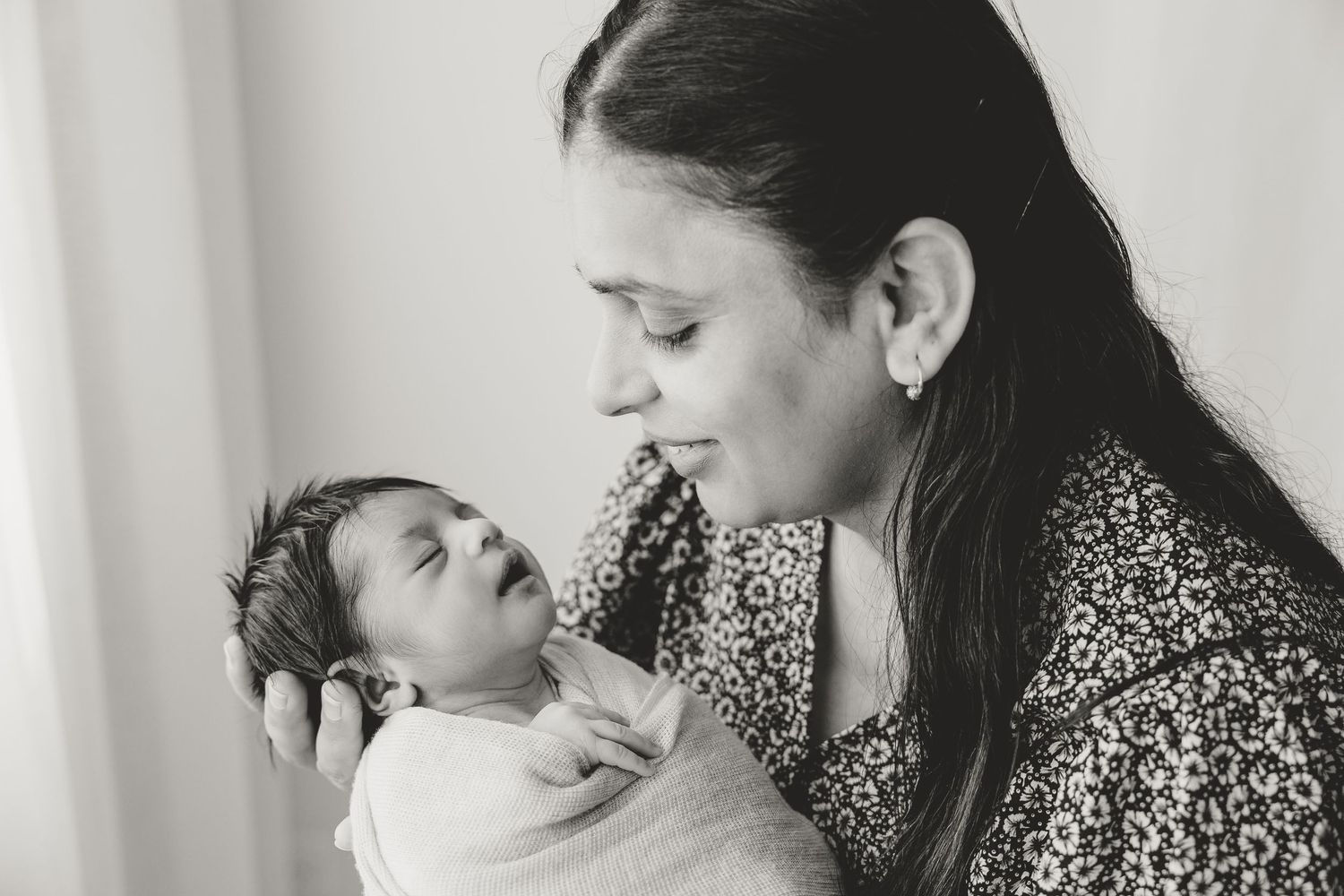 Black and white intimate photo of a mother cradling and gazing lovingly at their newborn baby. Natural family photography Tauranga
