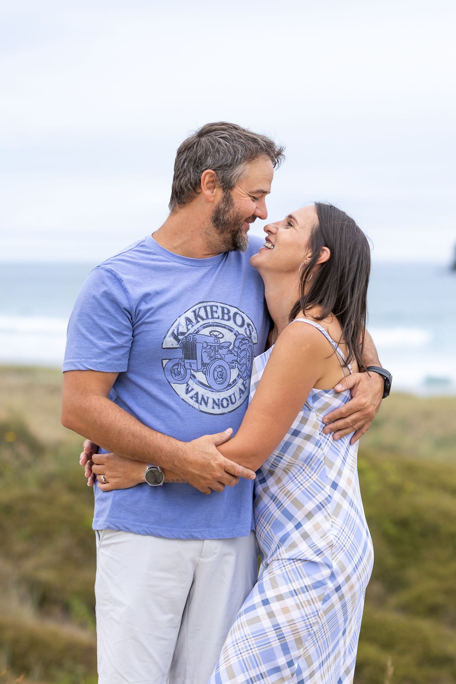 Happy couple sharing intimate moment on grassy coastal overlook.
