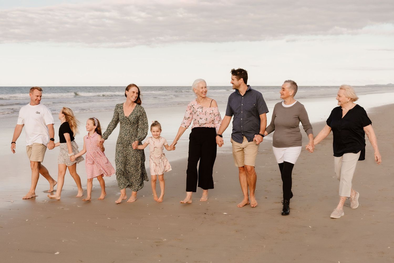 A group walks hand in hand along a sandy beach at sunset creating footprints in the sand.