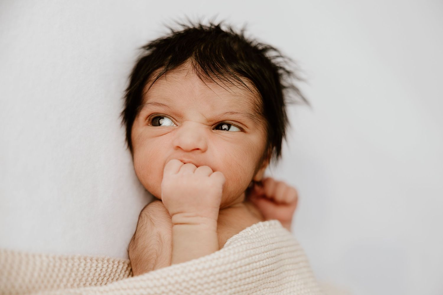 Baby making expressive faces while lying on white bedding in natural light.