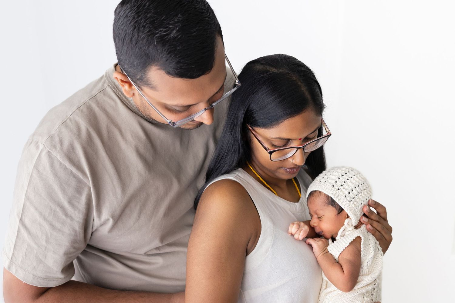 Parents sharing tender moment with their newborn in minimalist setting.