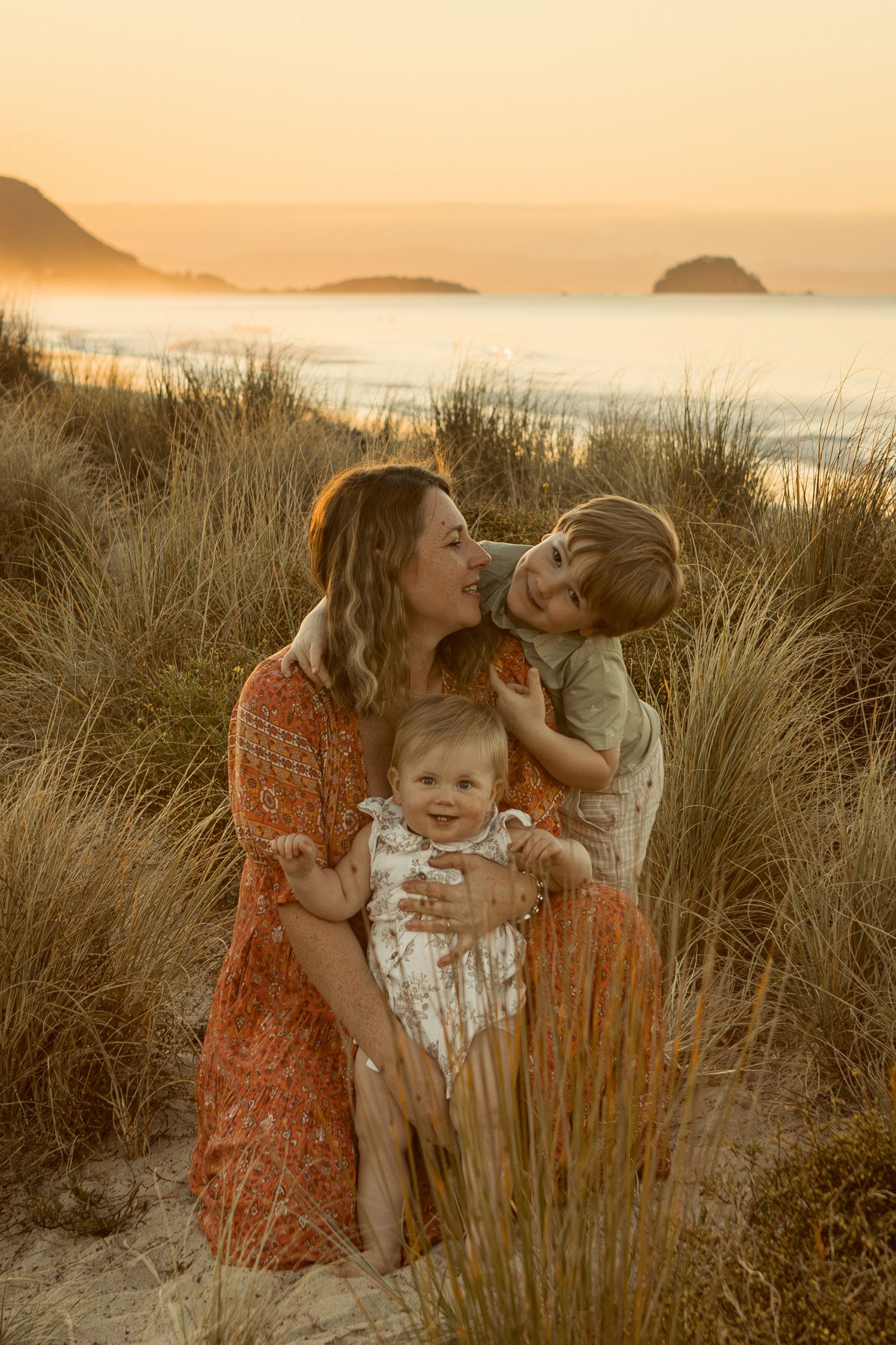 A tender family moment captured in golden light among coastal grasses at sunset.