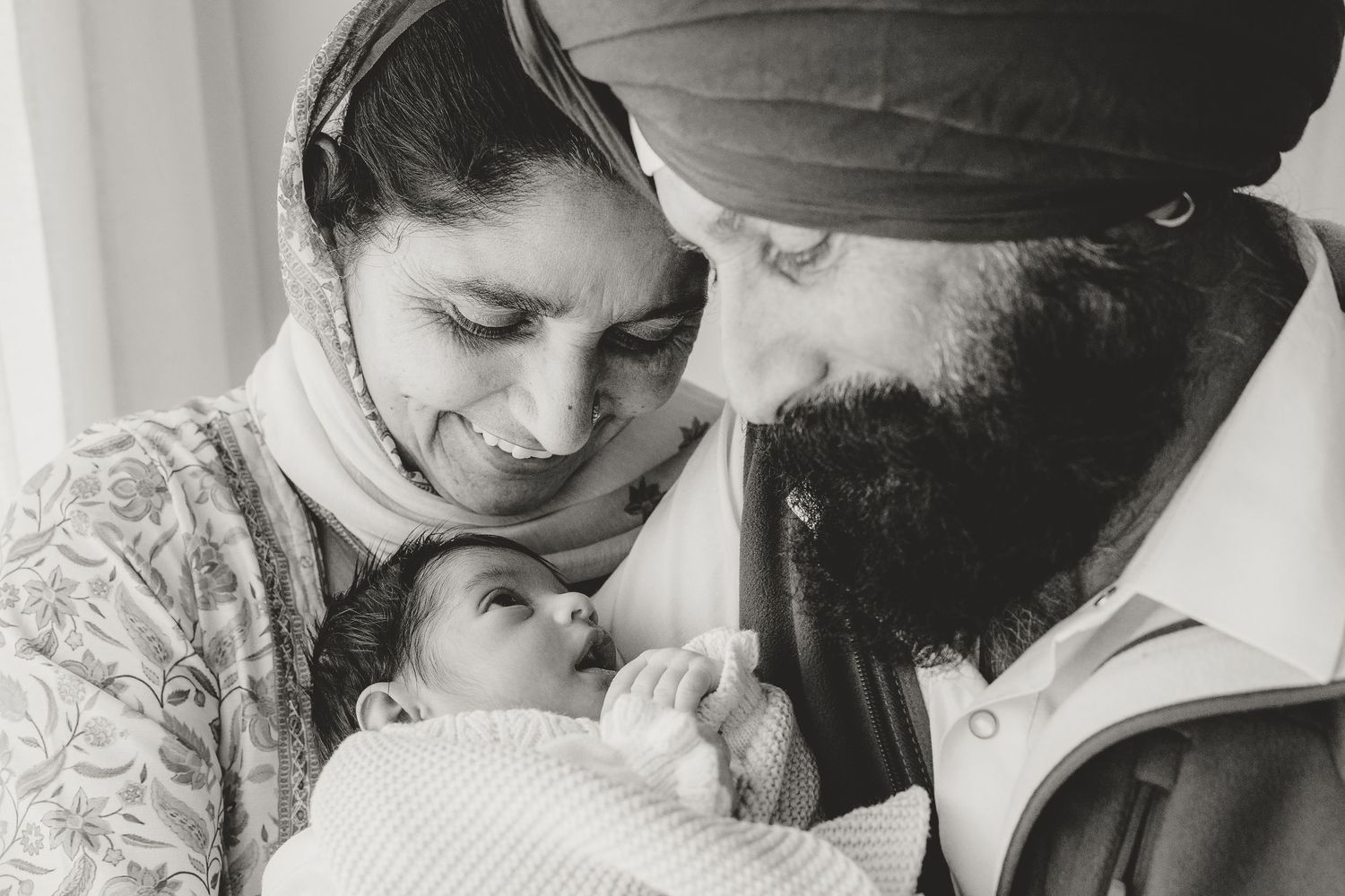 A loving family moment shared between parents and their newborn baby wrapped in a white blanket.