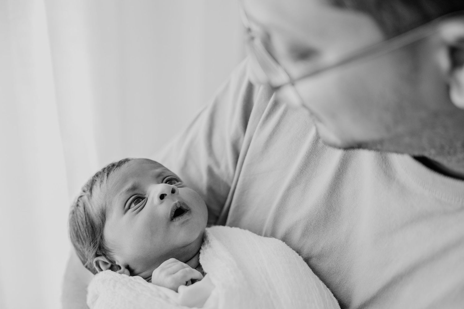 Parents in casual attire embracing their newborn in intimate black and white portrait.