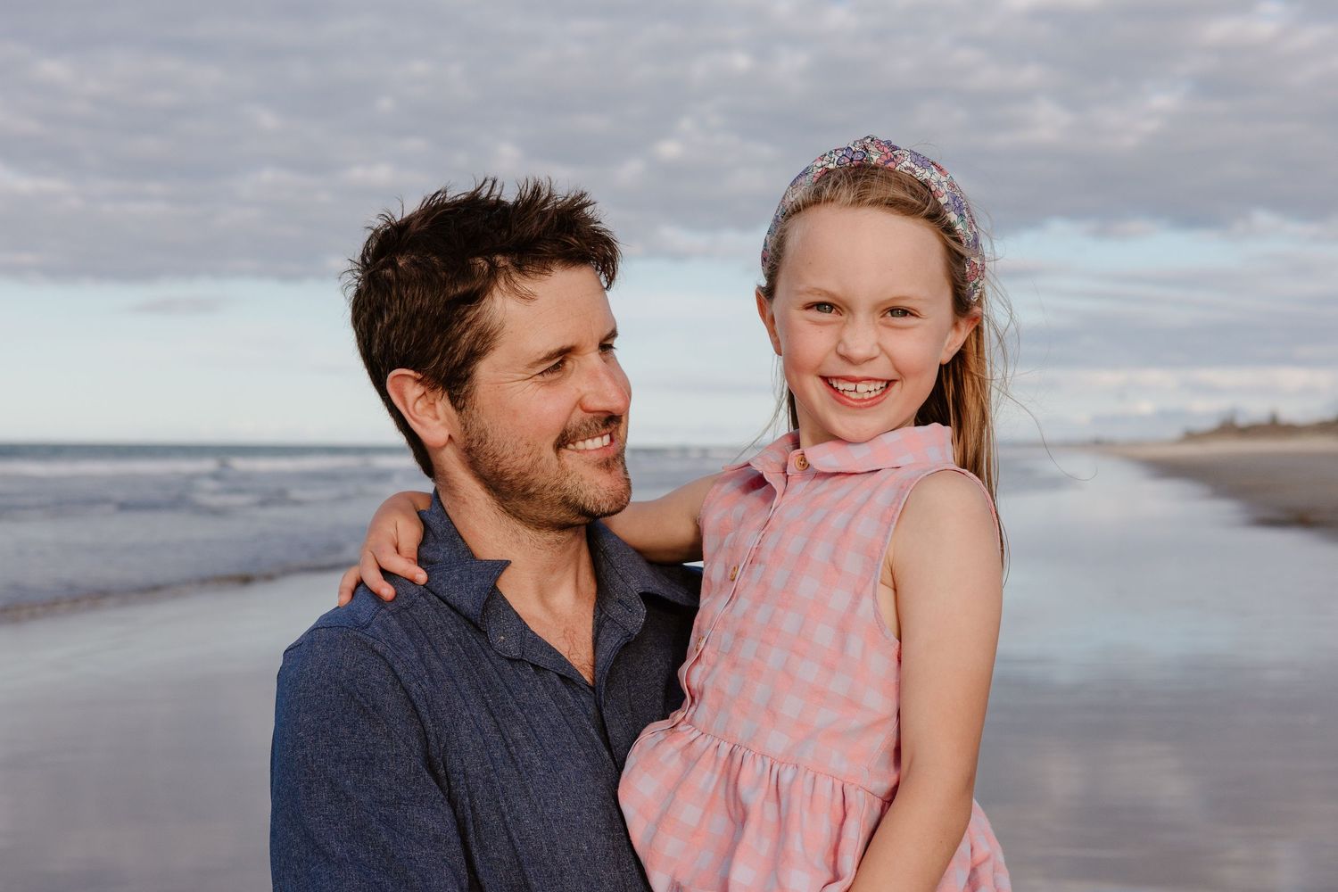 Parent and child enjoying a tender moment together on beach during cloudy day.