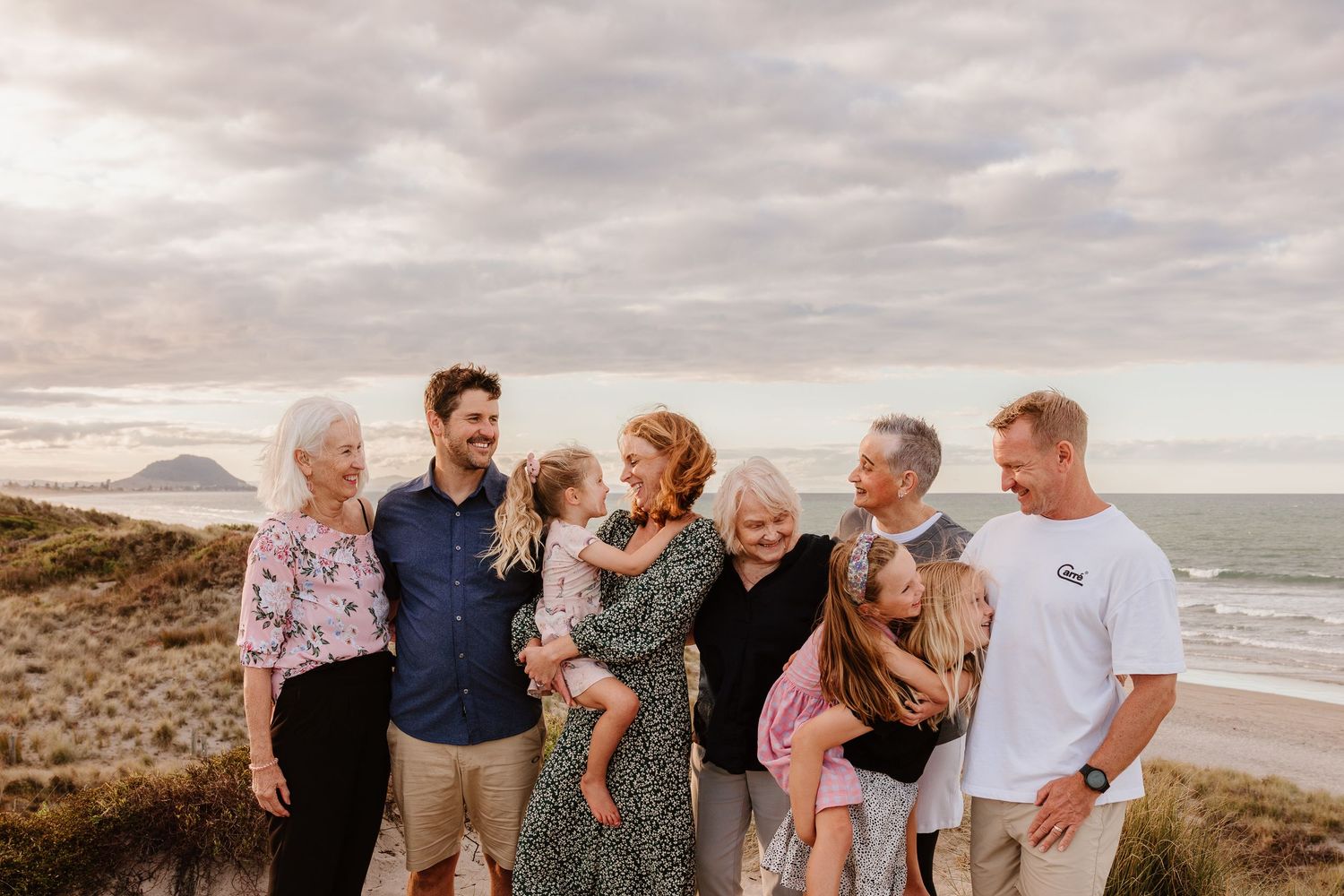 Multi-generational family gathering on coastal hilltop with ocean view.
