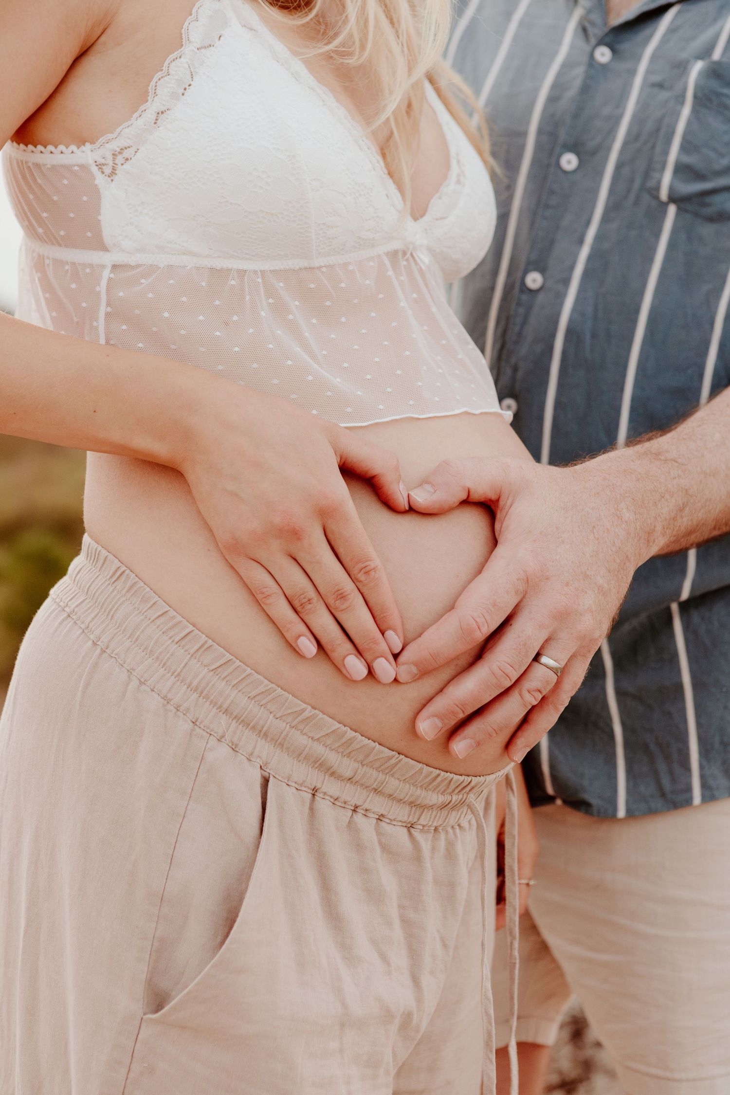 Close-up of hands cradling a pregnant belly in soft natural light.