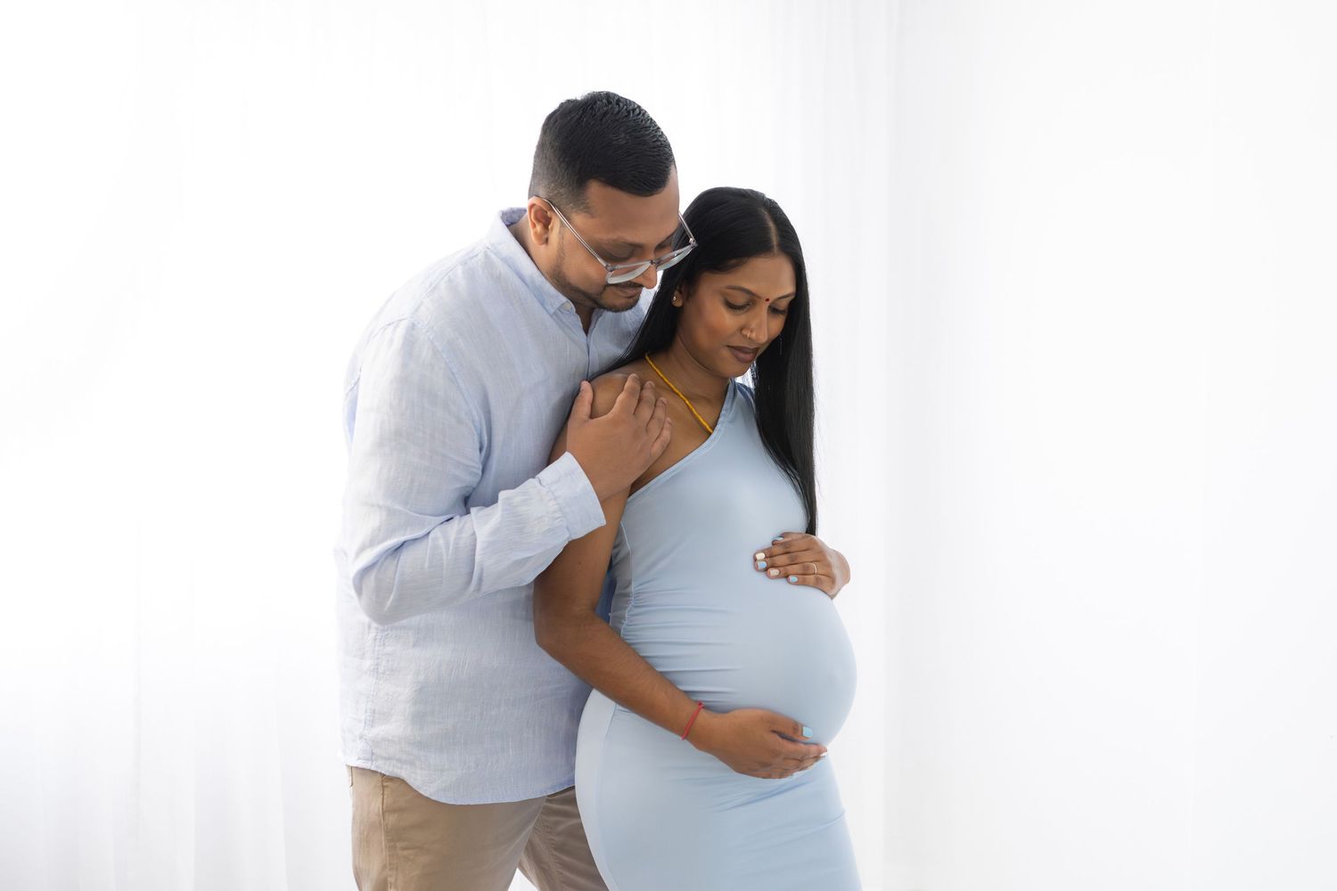 Intimate maternity portraits showing couple embracing against white backdrop.