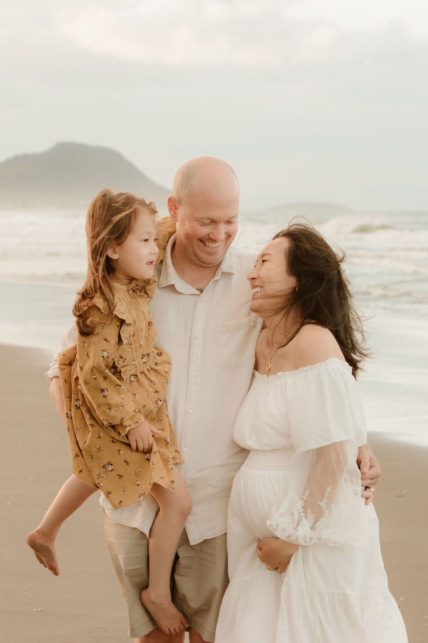 Family shares candid laughing moment together on windswept beach.