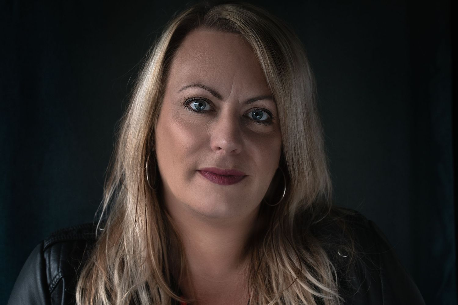 Portret van een vrouw tegen een donkere achtergrond met dramatische belichting en blond haar.