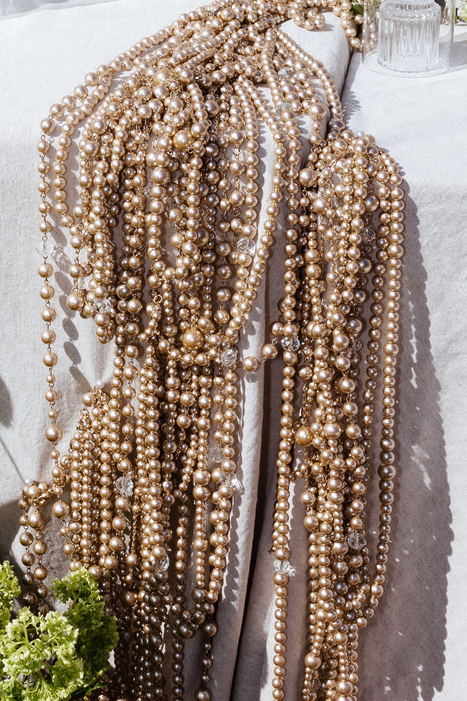 Long strands of champagne colored beaded pearl necklaces hanging against a white wall.