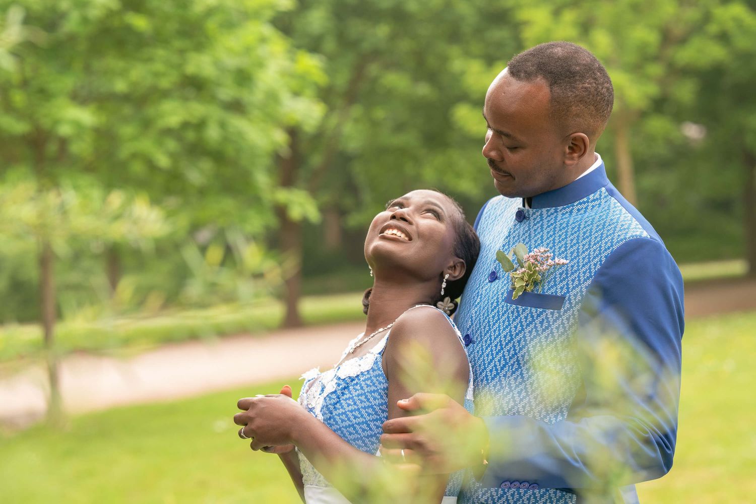 Joyful couple embracing outdoors in coordinating blue outfits during springtime celebration in park setting.