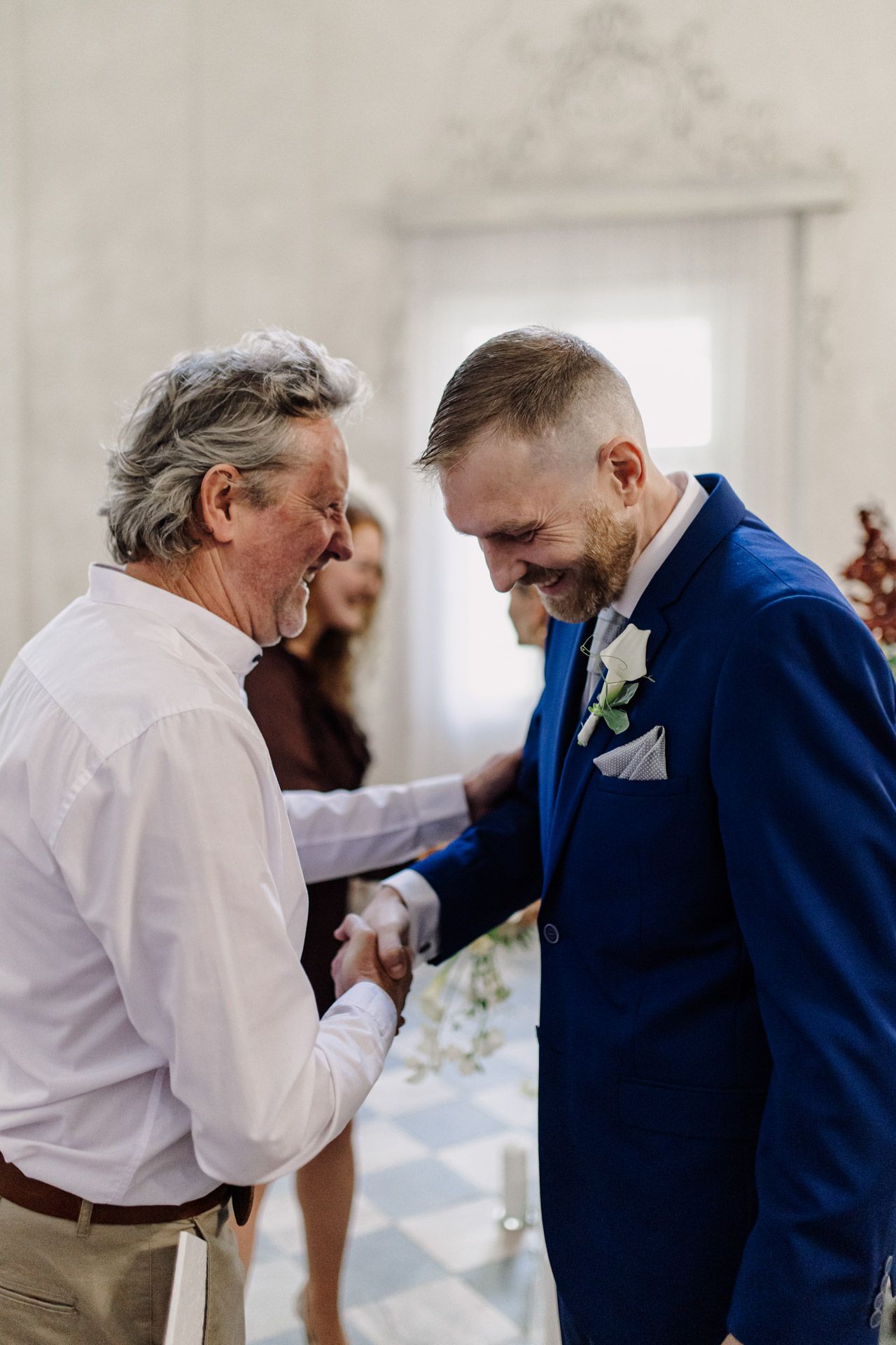 Emotional moment shared between wedding guest and groom in white interior.