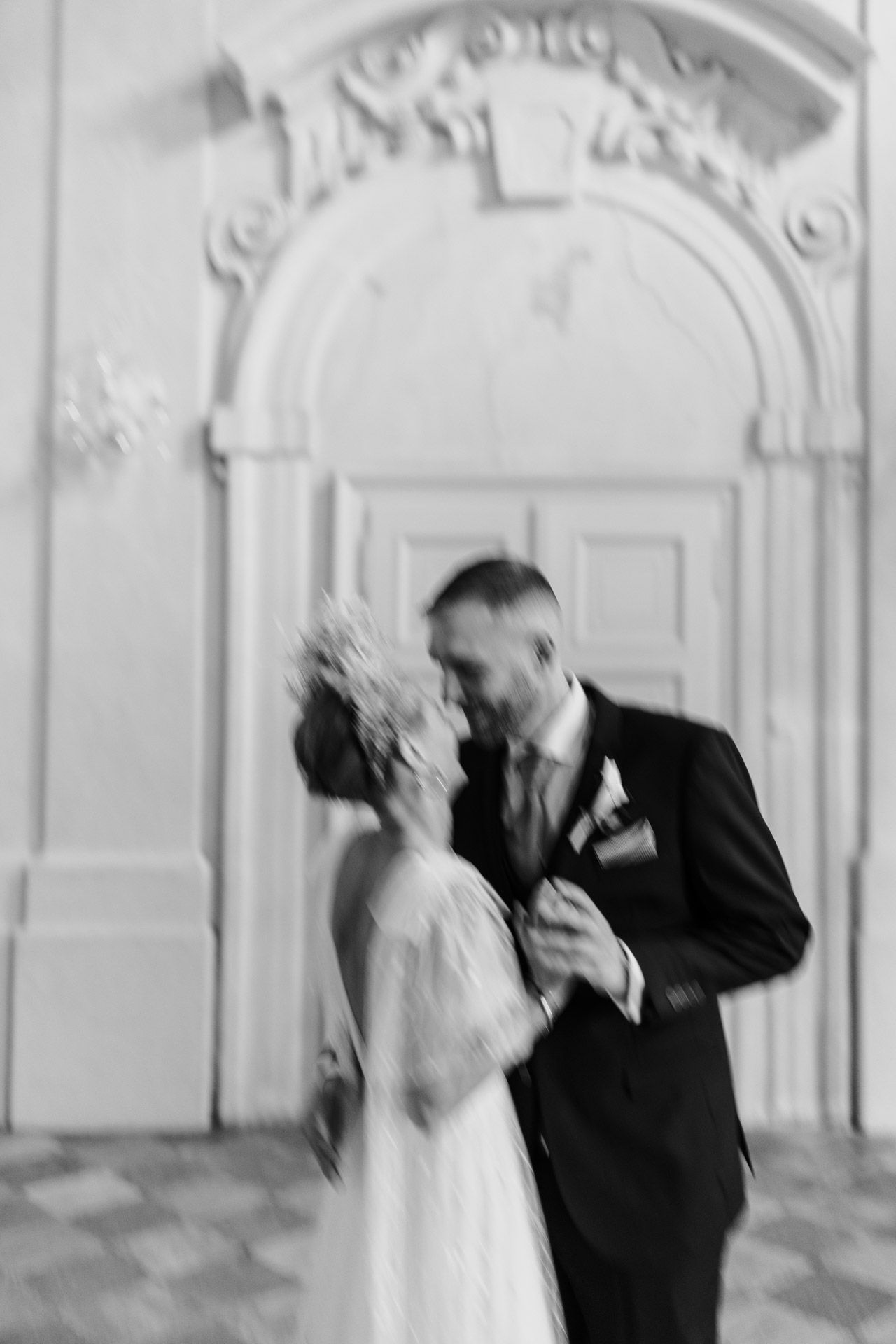 A romantic black and white wedding photo capturing a tender moment between newlyweds in front of an ornate archway.