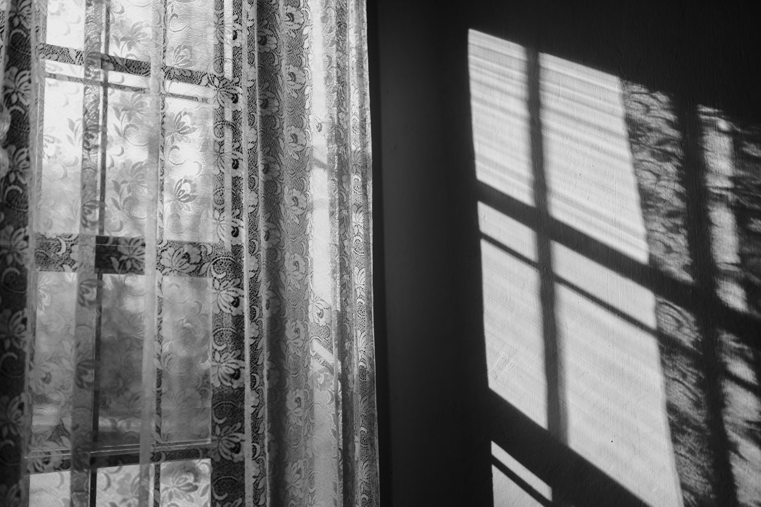 Artistic black and white photo of window light casting shadows through lace curtains.