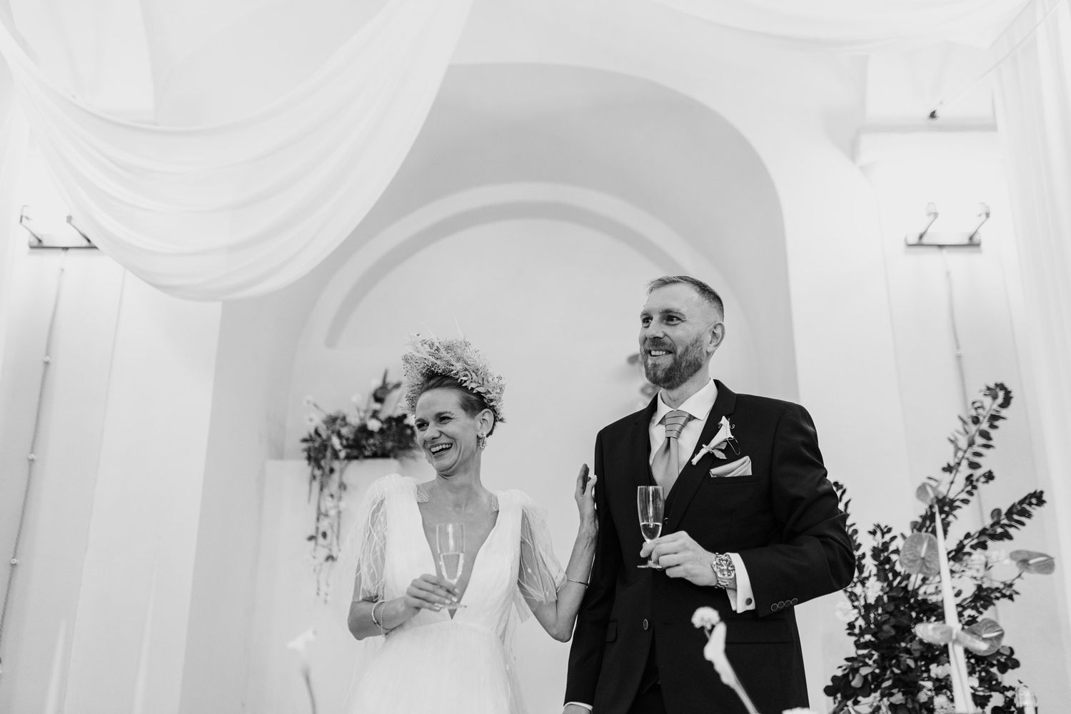 Wedding couple sharing a joyful laugh during ceremony in elegant white arched venue.