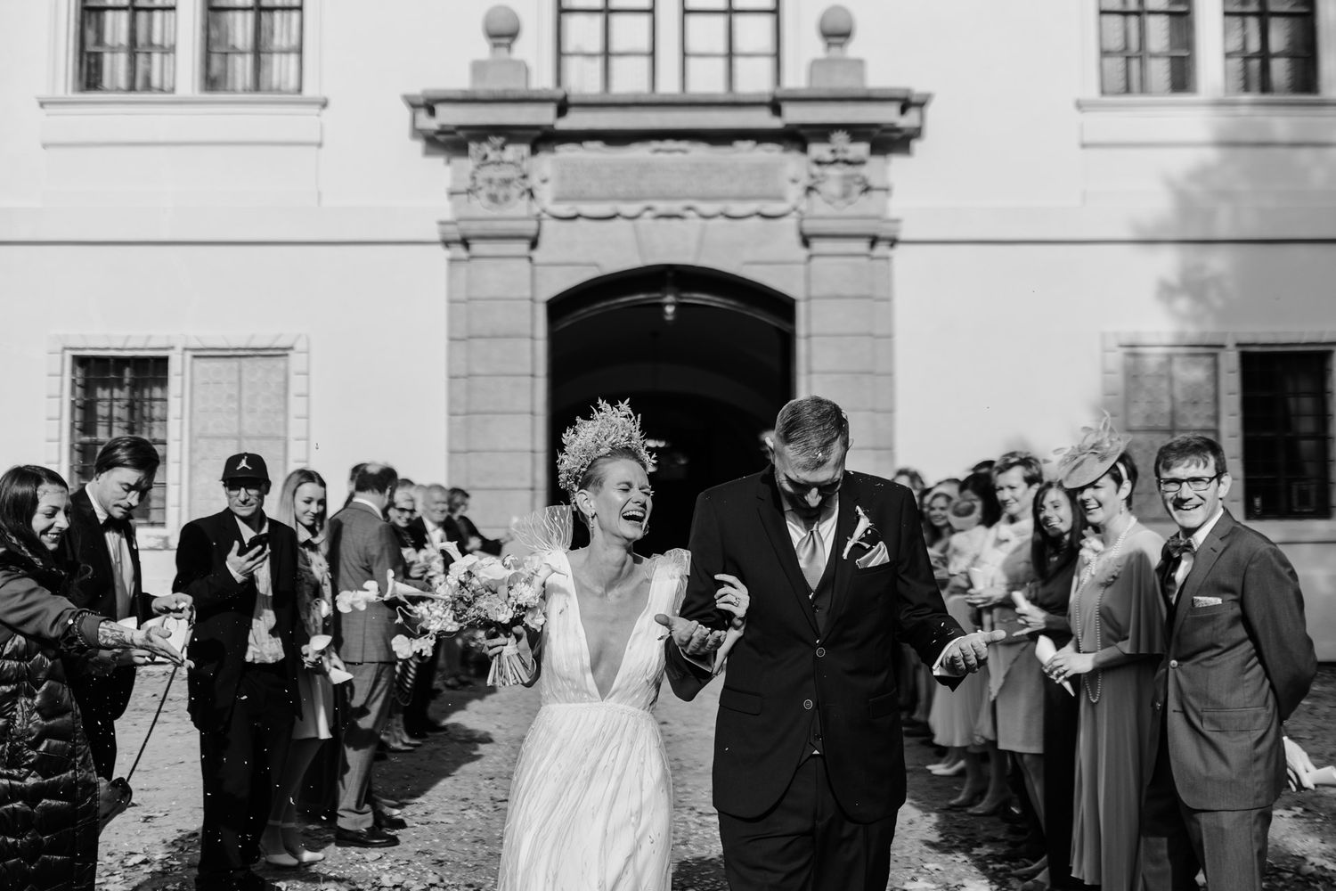 Black and white photo of wedding celebration with guests showering confetti at ornate building entrance.