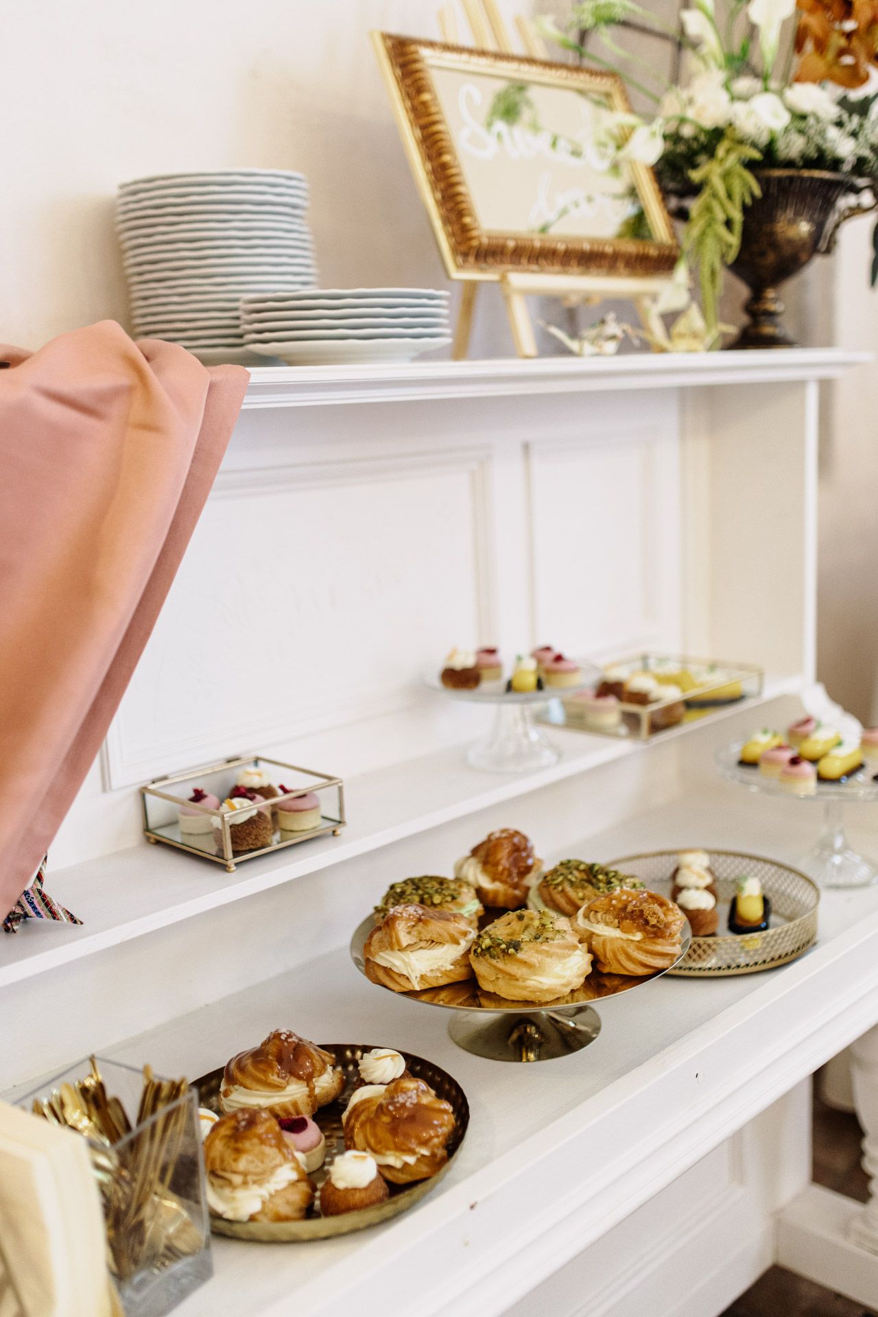 Elegant buffet display with stacked plates and pastries on white shelving.