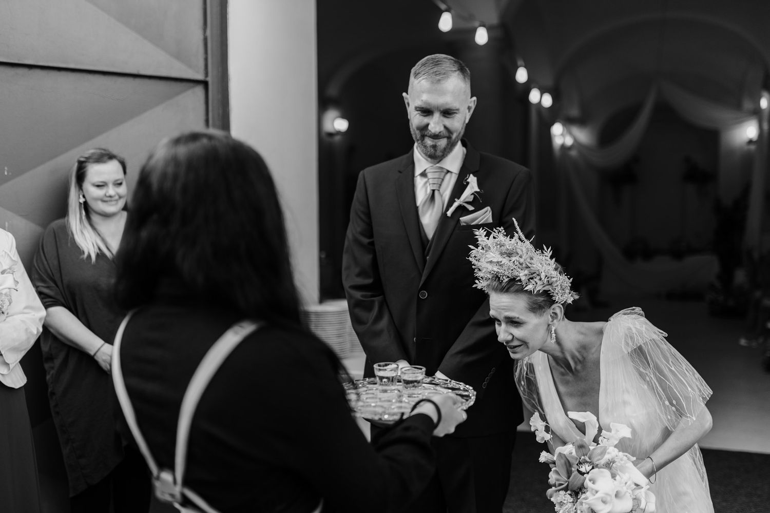 Black and white candid reception moment with guests gathered around tables.