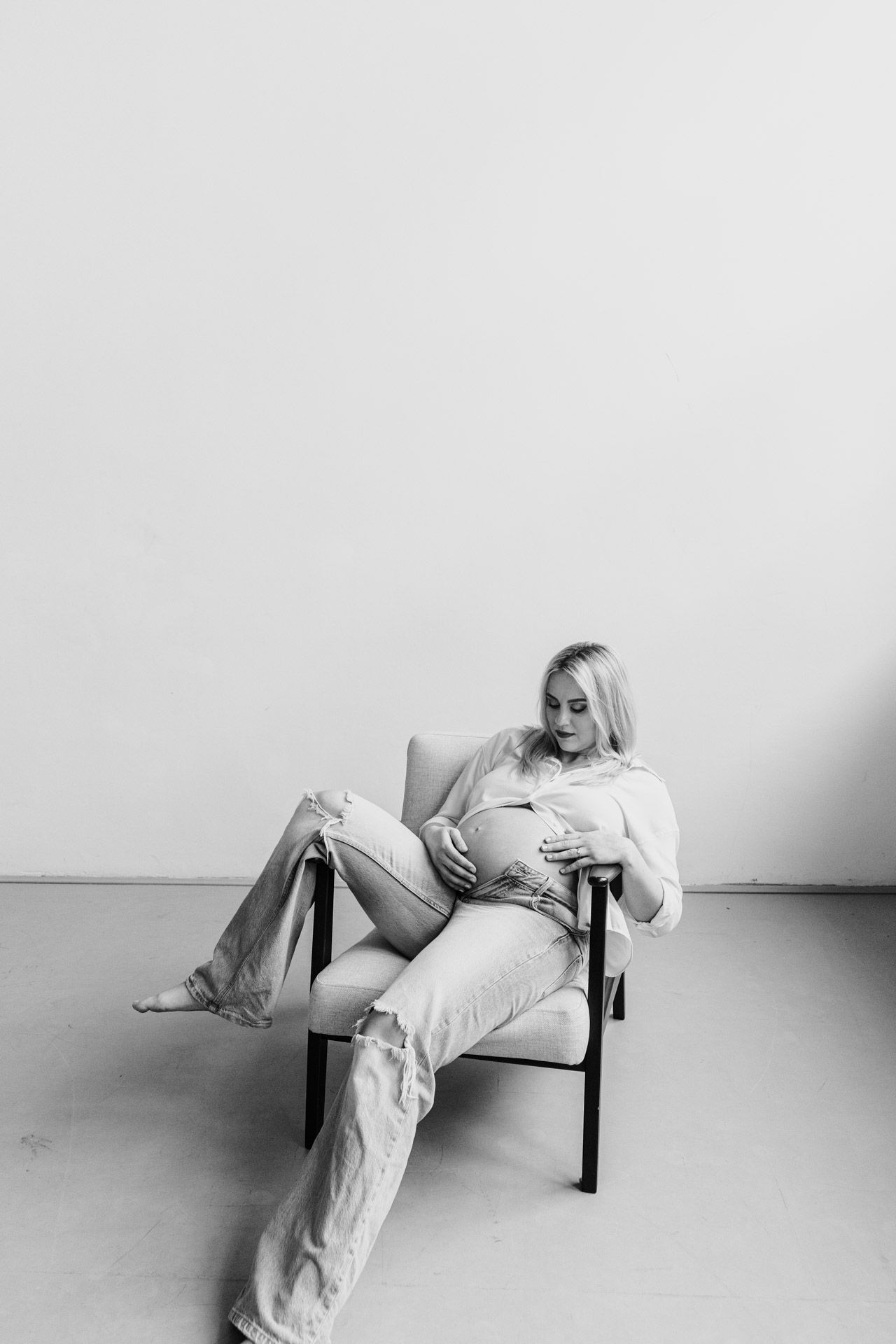 Black and white artistic portrait of someone lounging barefoot in a chair wearing casual light-colored clothing.