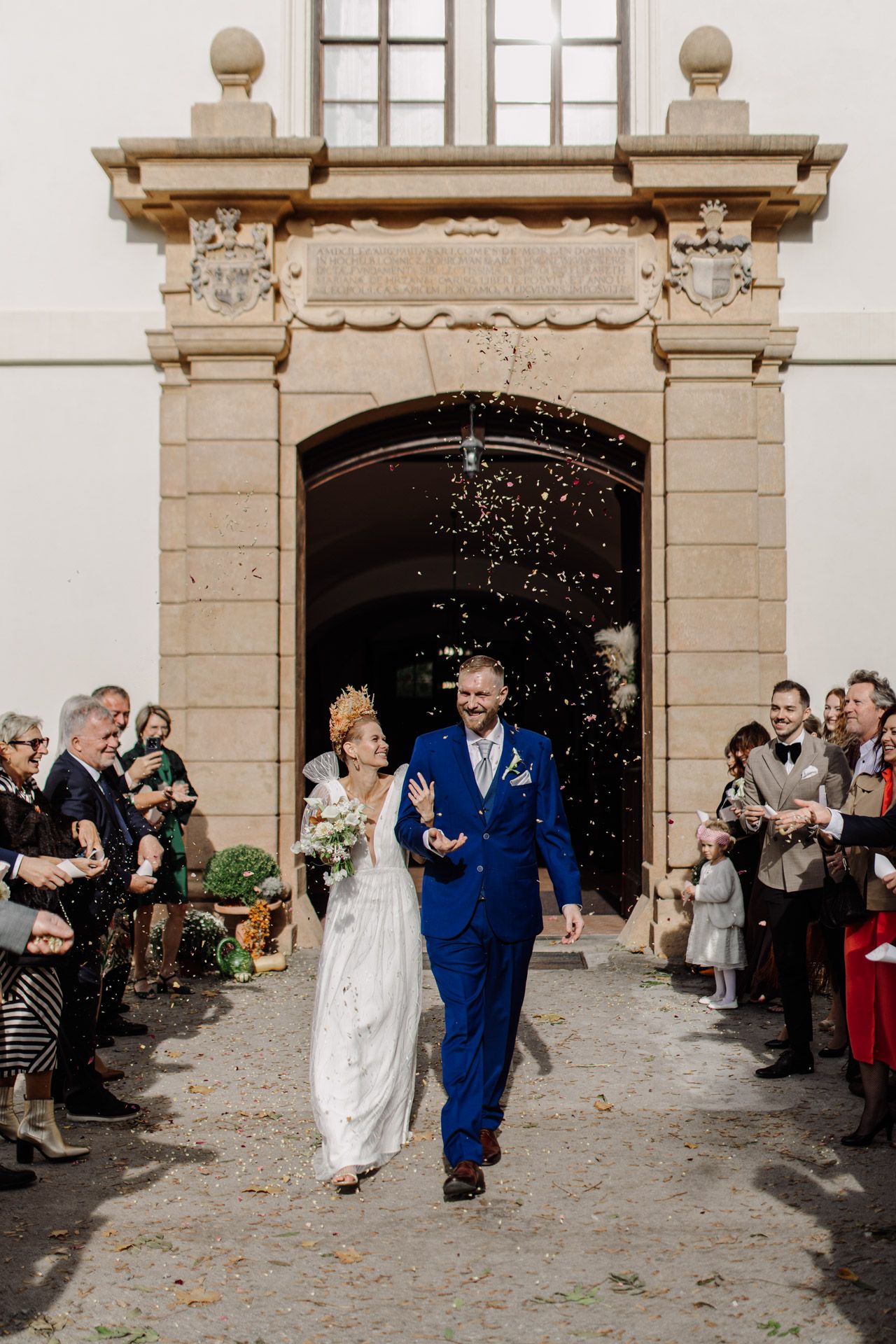Photo of wedding celebration with guests showering confetti at ornate building entrance.