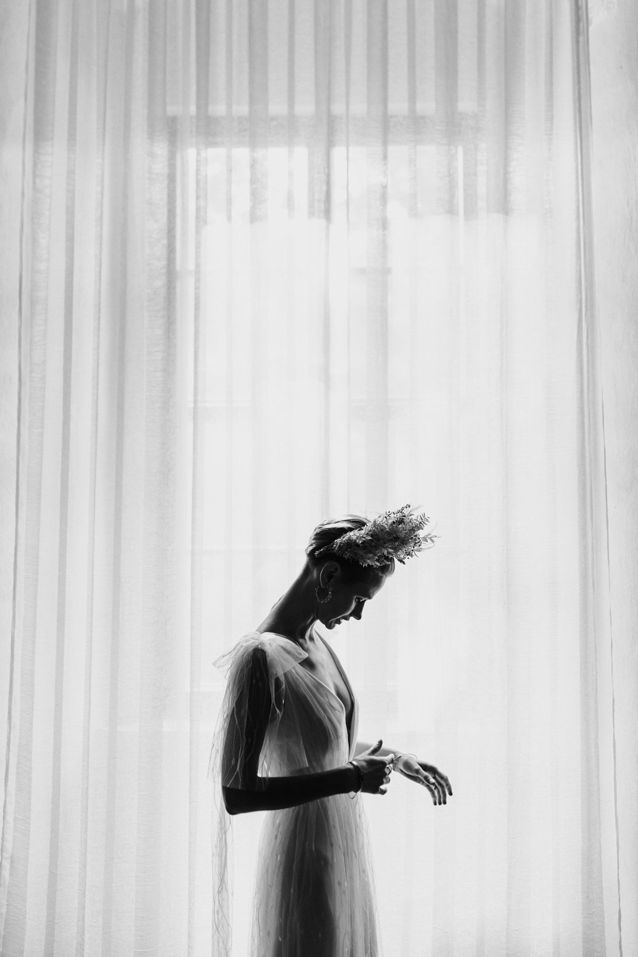 Black and white silhouette of person in dress against sheer curtains in dramatic lighting.