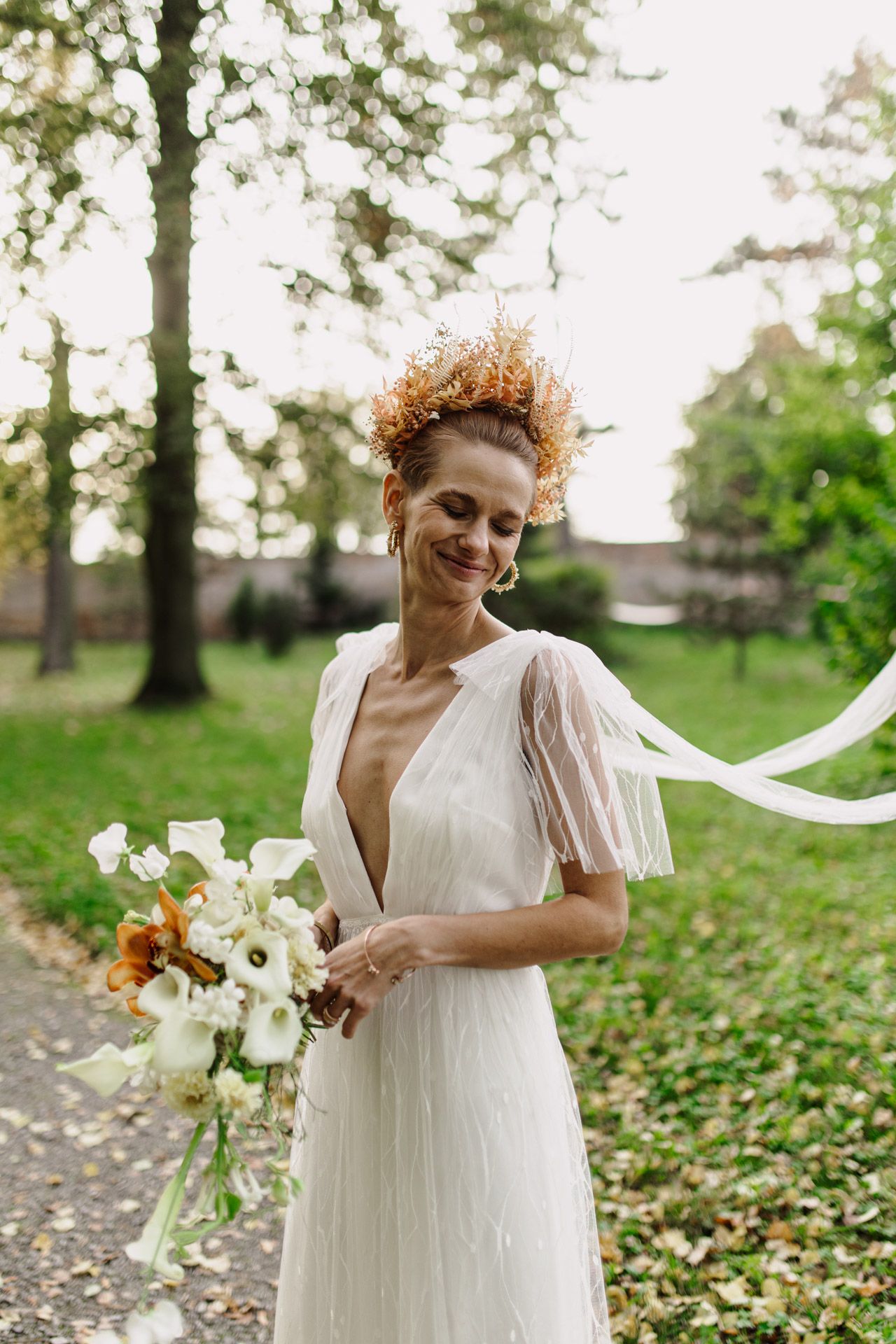 Bride in flowing white dress with flutter sleeves holds bouquet of white flowers in outdoor garden setting.