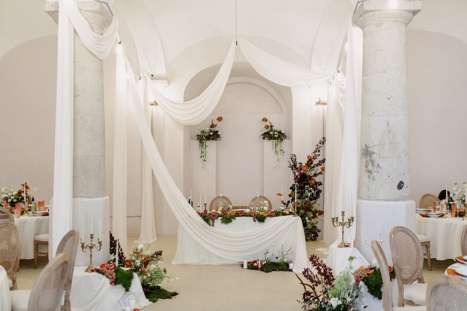 Elegant white wedding reception venue decorated with flowing fabric drapes and floral arrangements.