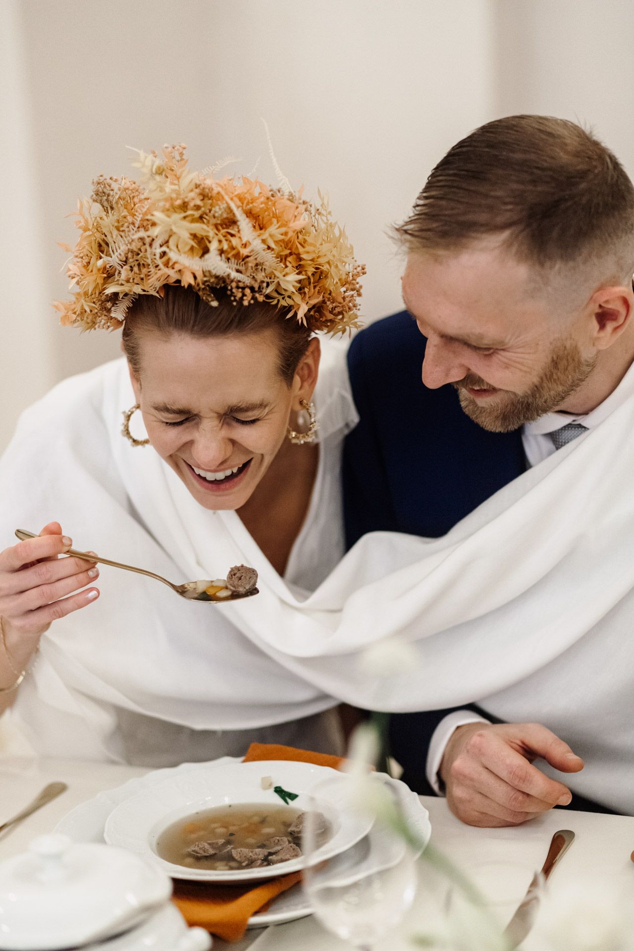 Newlyweds enjoying meal together while wrapped in cozy white blanket.