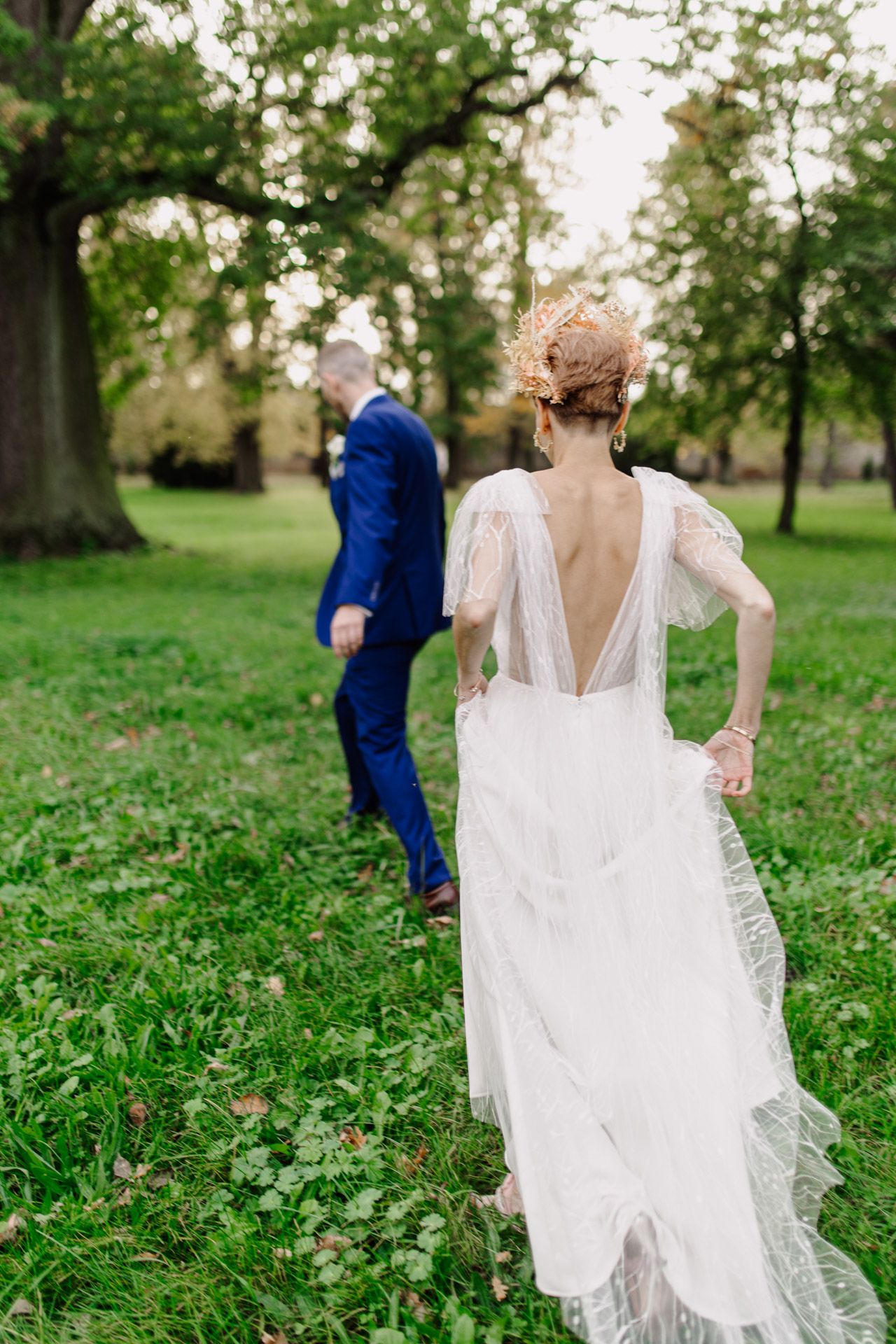 Elegant wedding dress with sheer back detail shown as couple stands in lush garden setting.