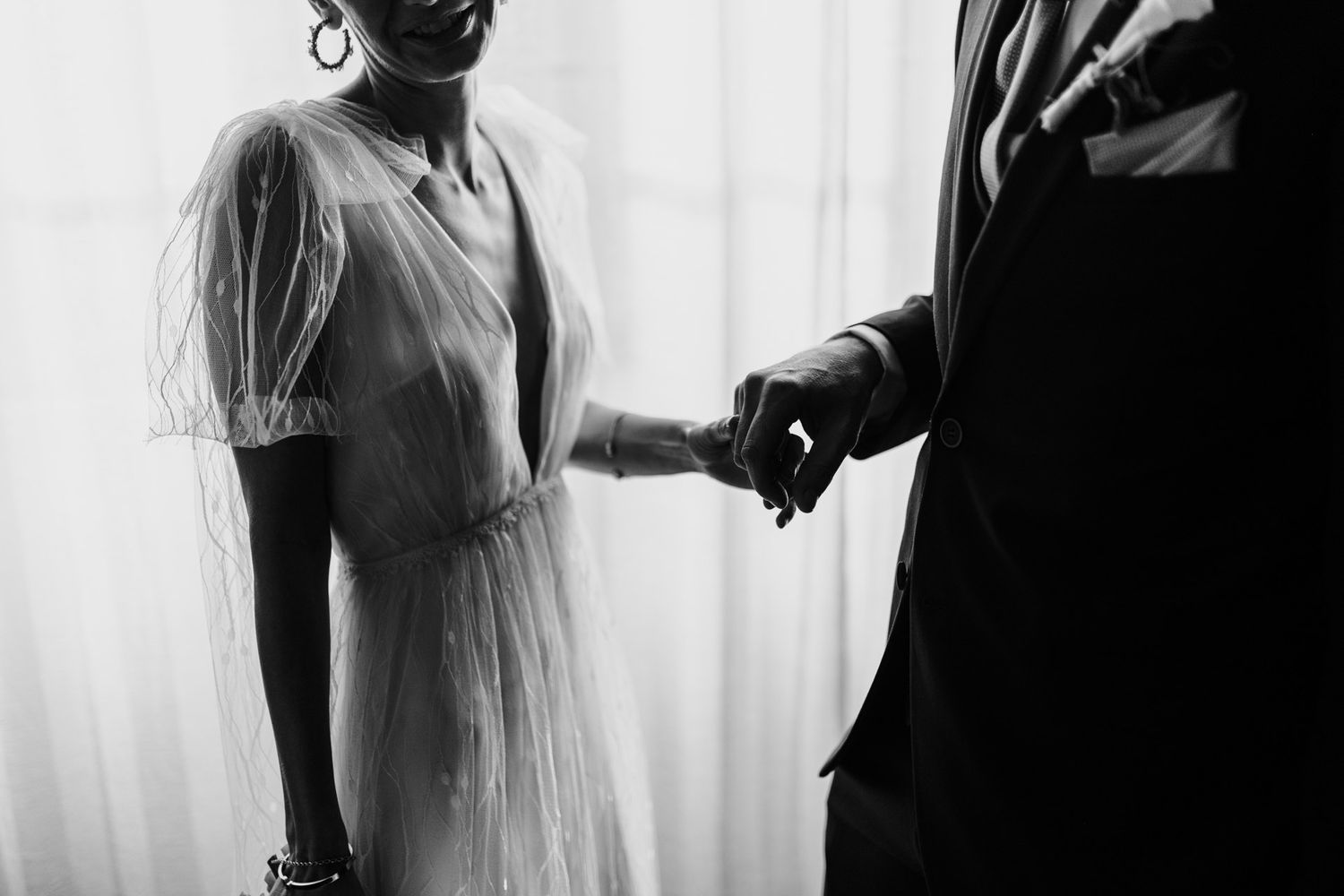 Black and white artistic photo of couple holding hands in vintage-style wedding attire.