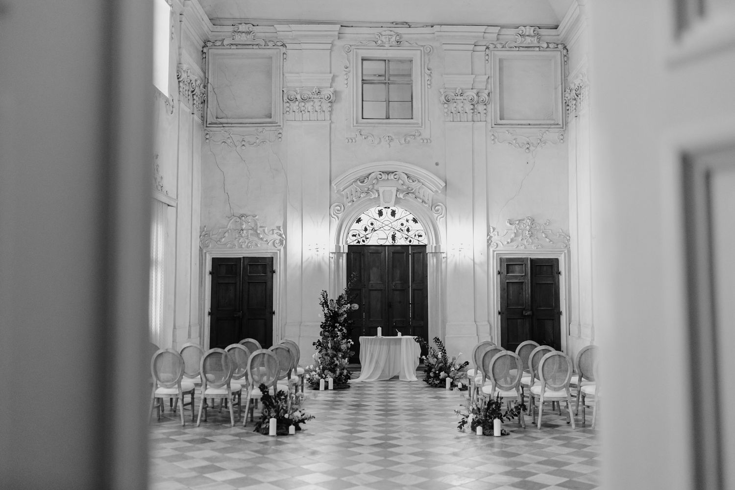 Elegant vintage hall with white walls, ornate molding, and cane chairs arranged for a formal ceremony.