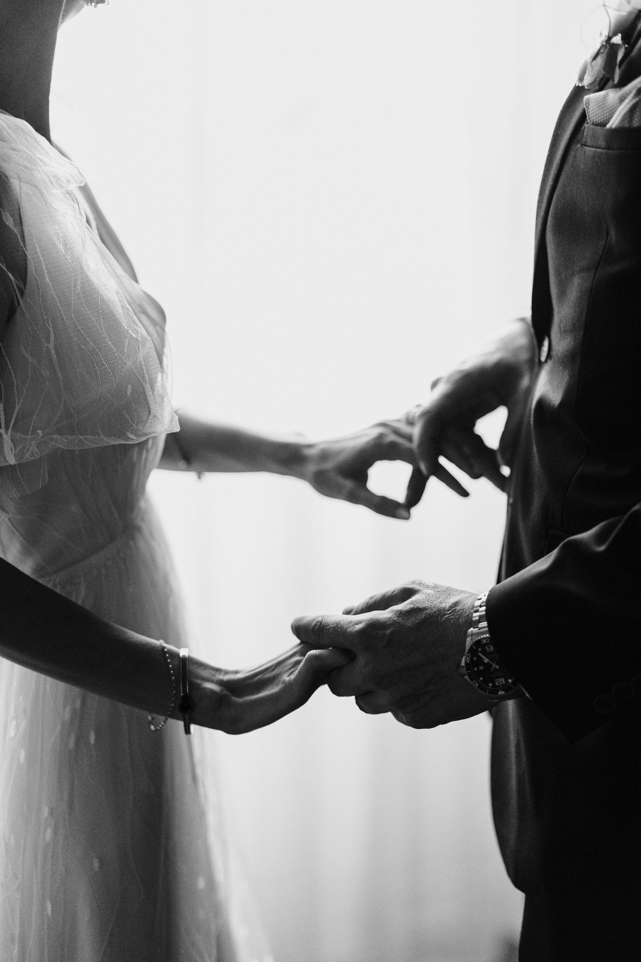 Intimate black and white photo of hands exchanging rings during wedding ceremony.